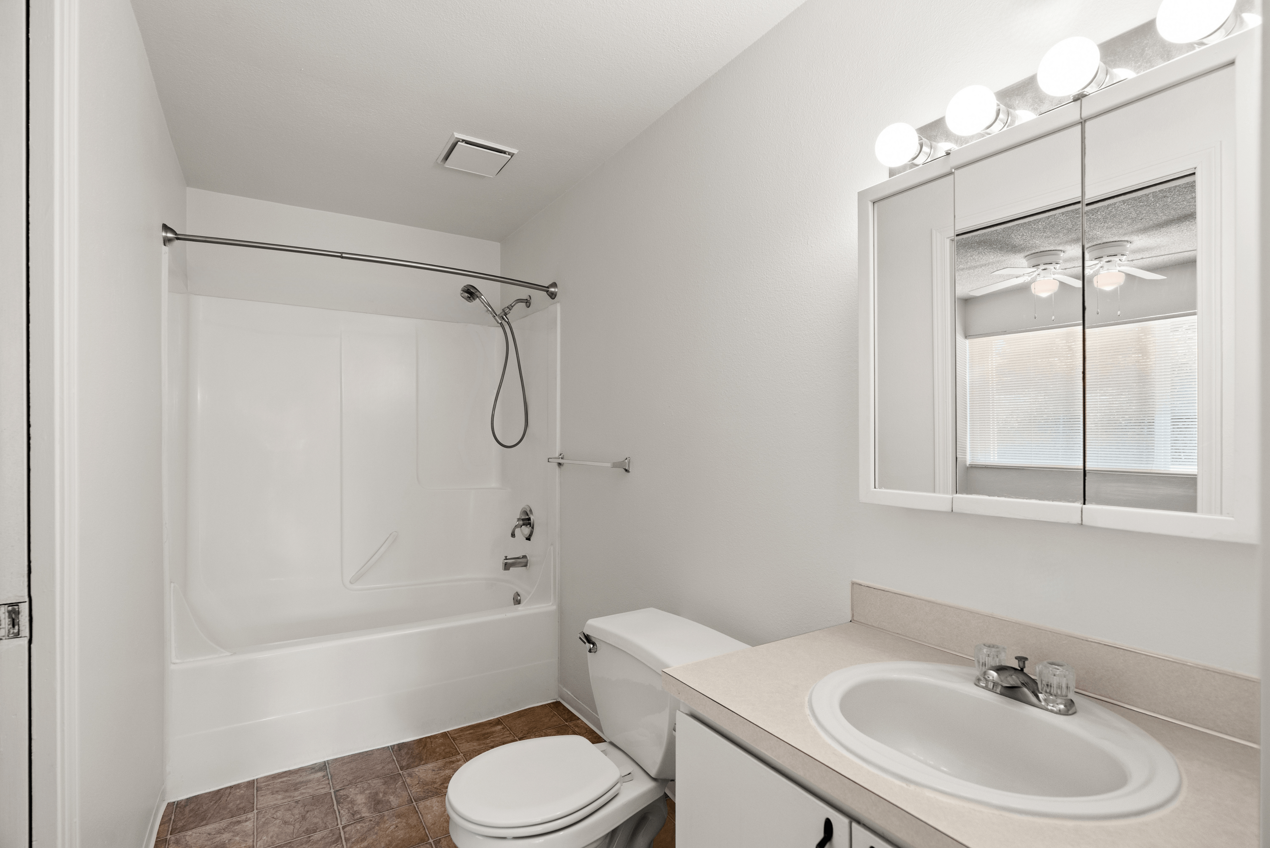 Modern bathroom featuring a sleek white bathtub with shower, stylish vanity with sink, and bright overhead lighting.