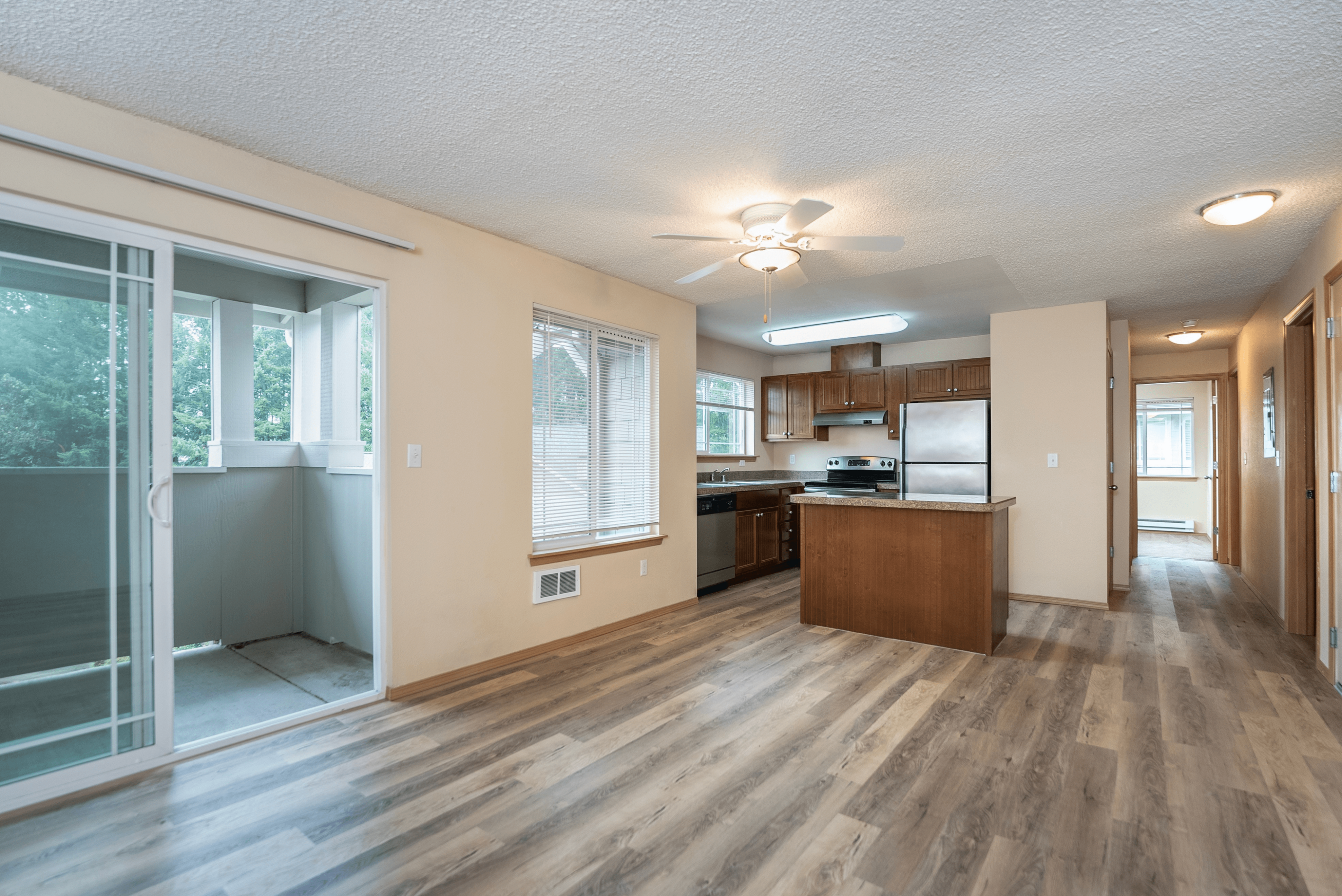Spacious open-concept kitchen and living area with wood flooring, a central island, and large windows providing natural light. Sliding glass door leads to a private balcony.