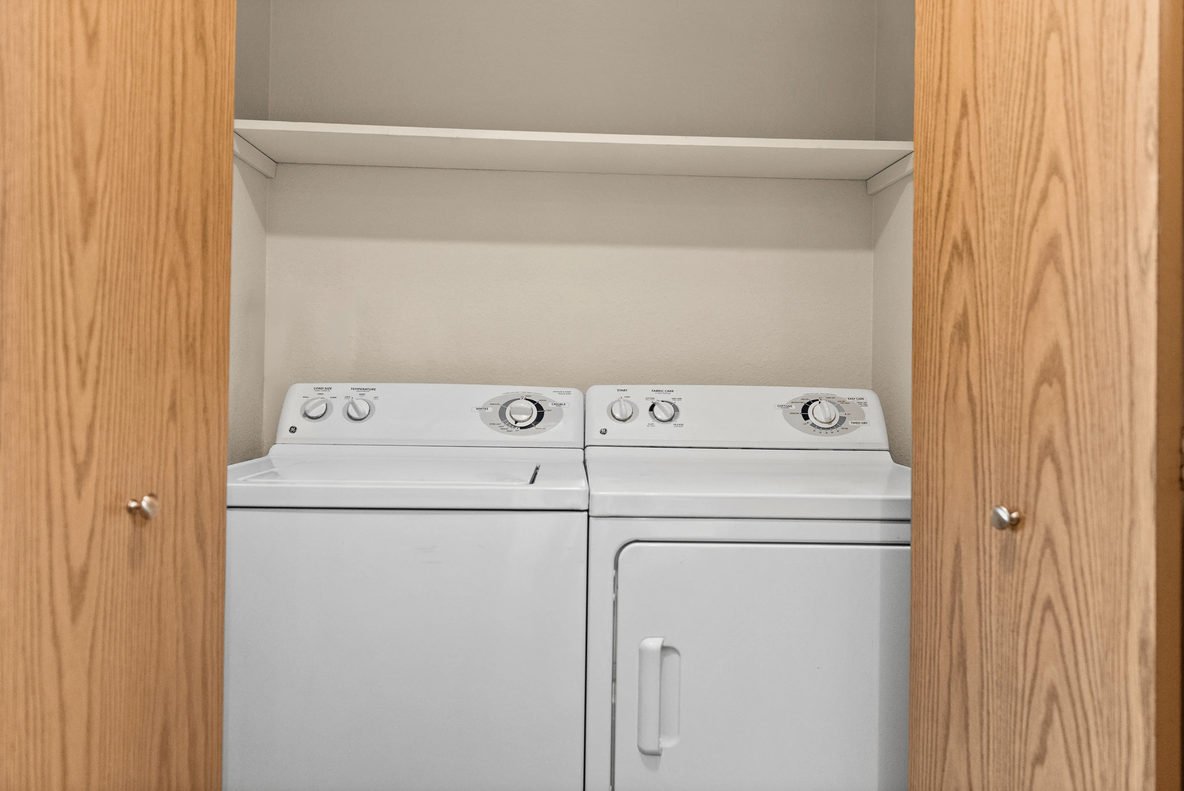 Convenient in-unit laundry with washer and dryer, neatly tucked behind wooden cabinet doors.
