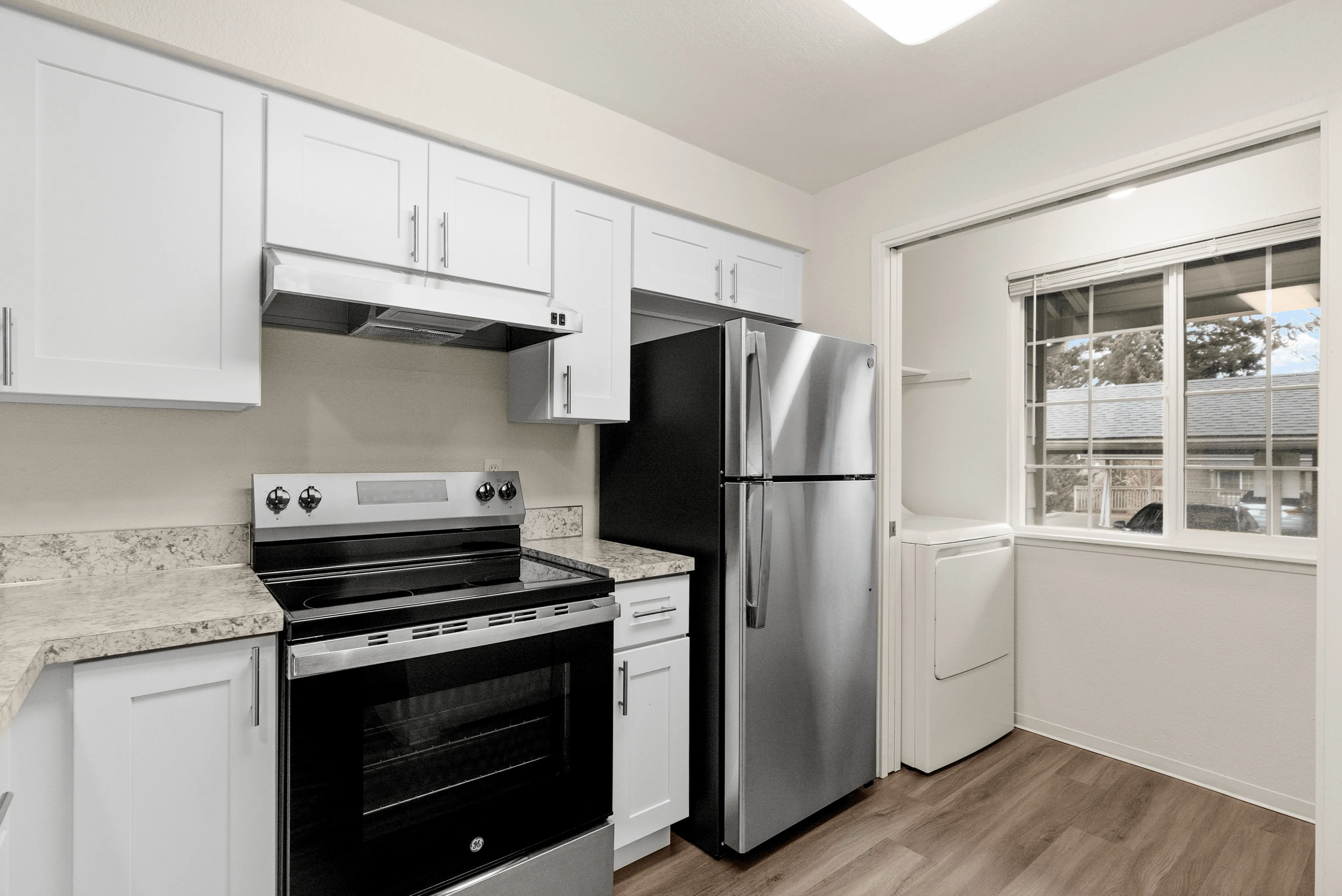 Modern kitchen with sleek stainless steel appliances, white cabinets, and large window for natural light.