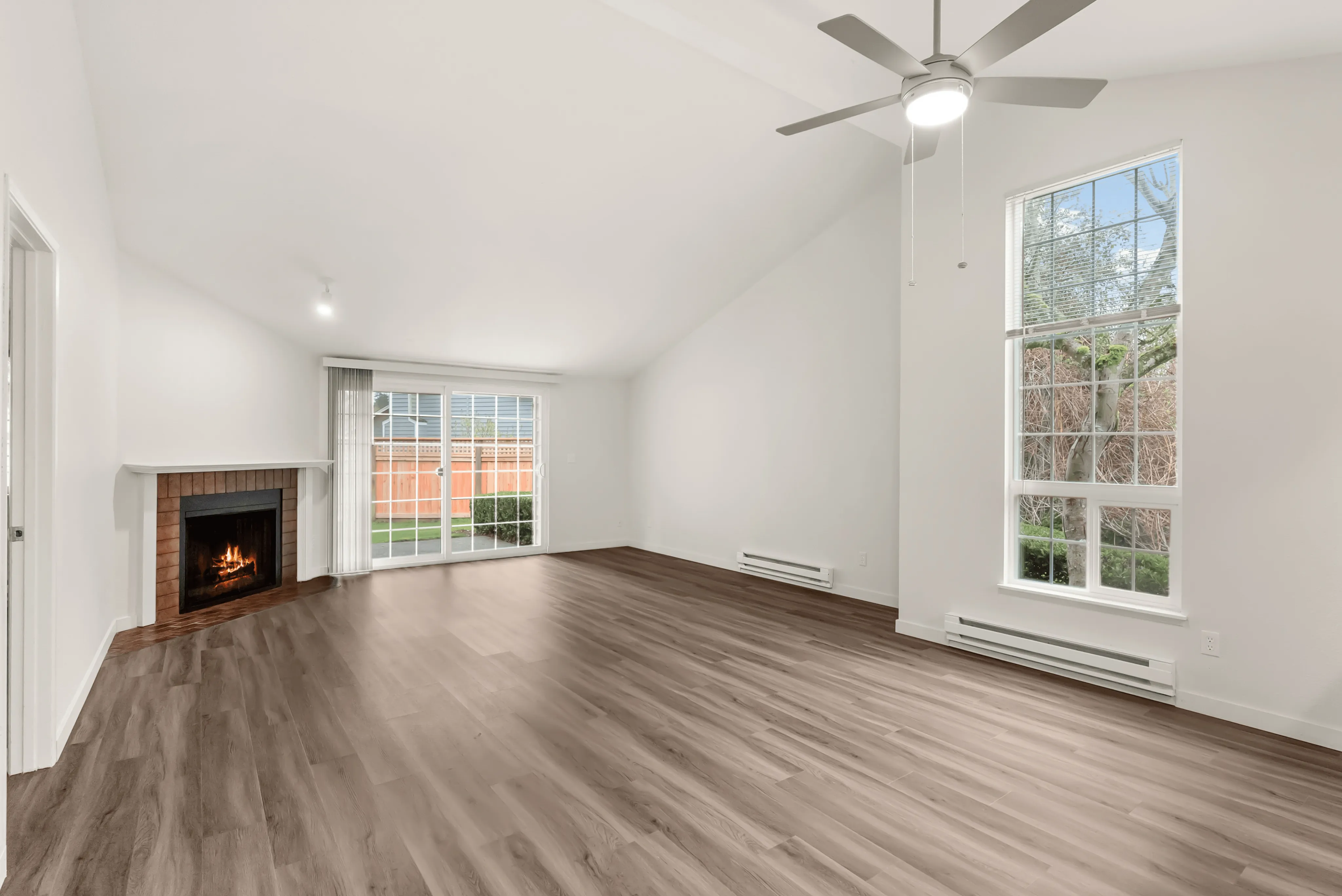 Bright and airy living room with a cozy fireplace, modern ceiling fan, and large windows overlooking a private garden.