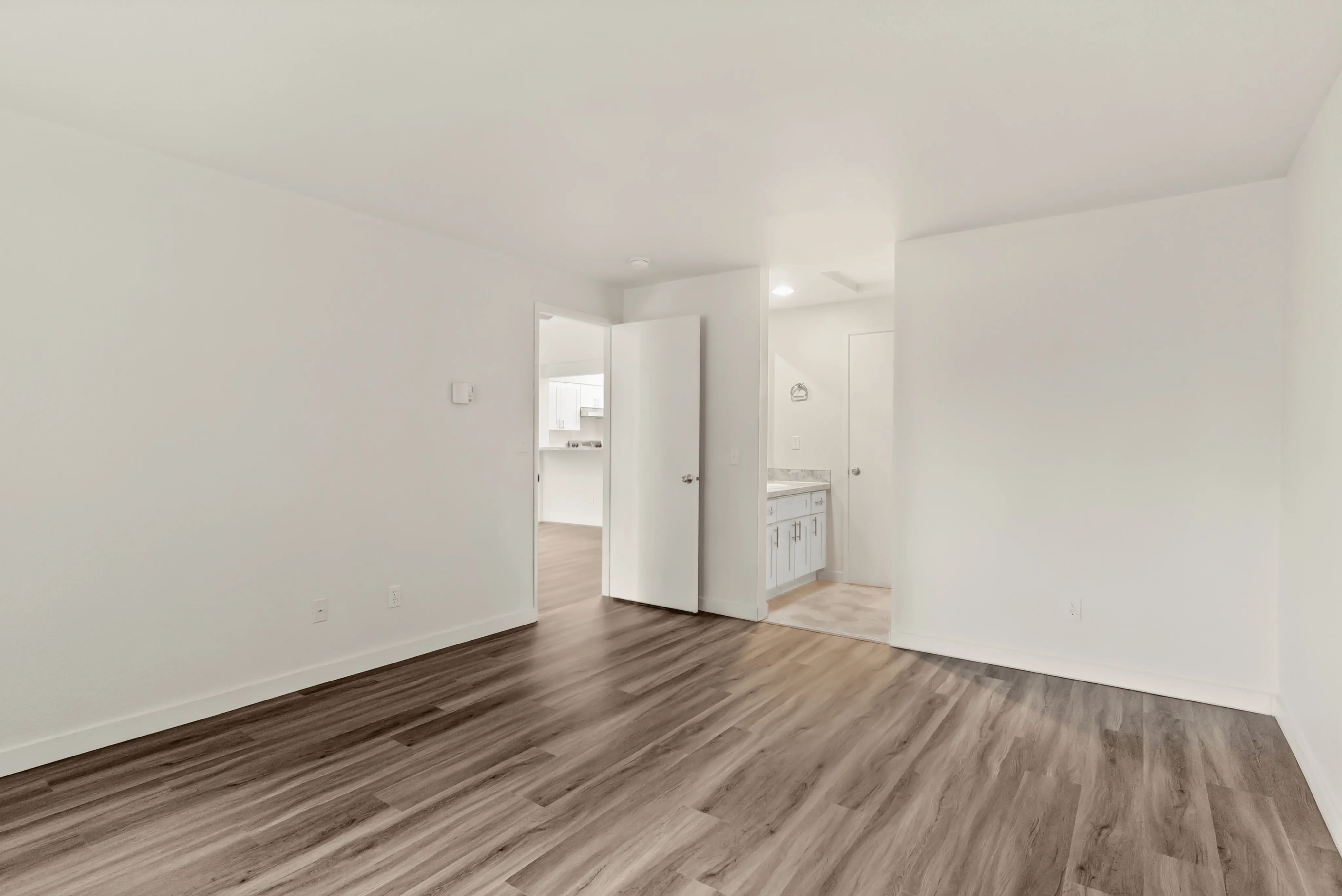 Bright, spacious room with elegant wood flooring leading to a modern kitchen and bathroom area.