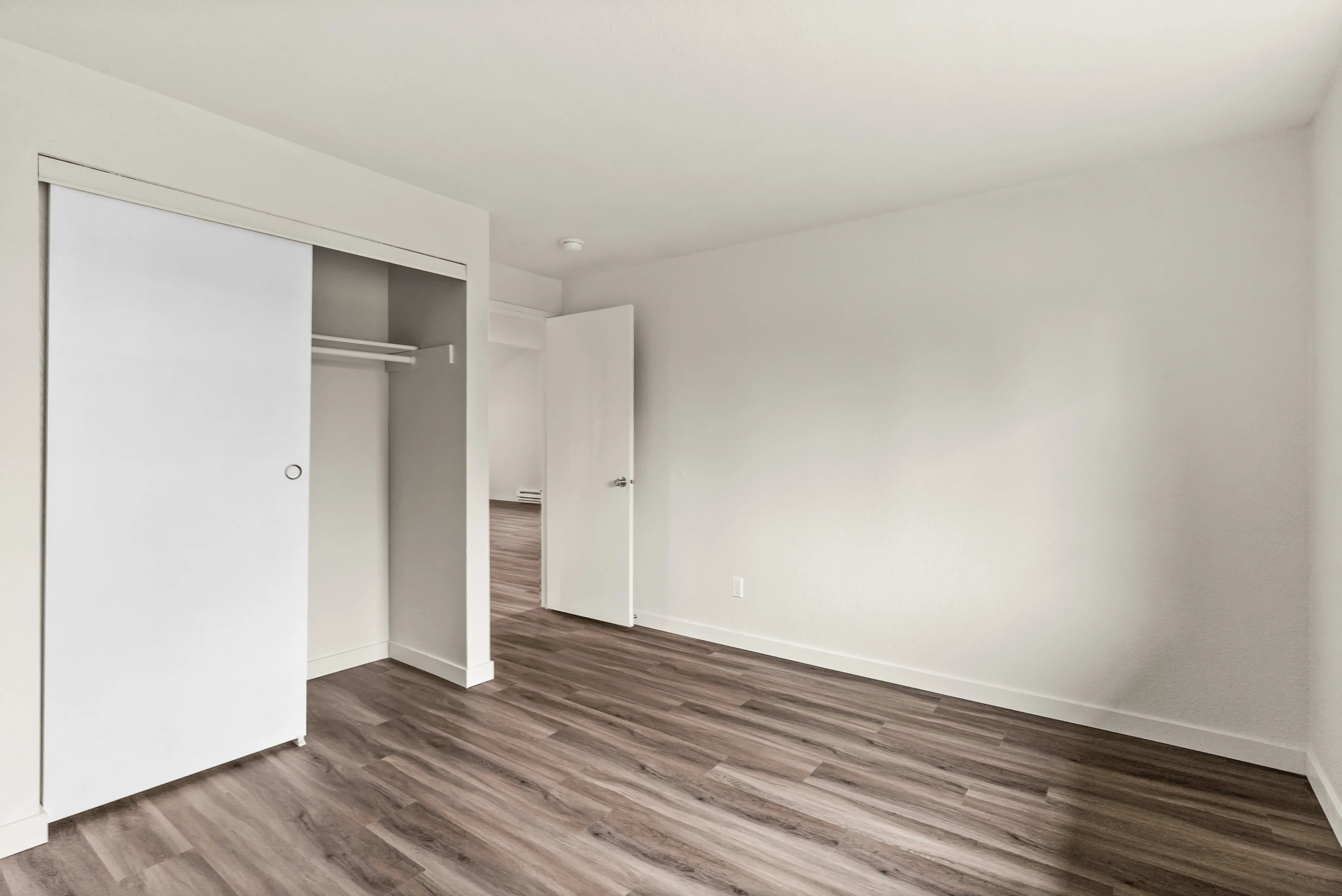 Spacious bedroom with elegant wood flooring and a large sliding closet door.