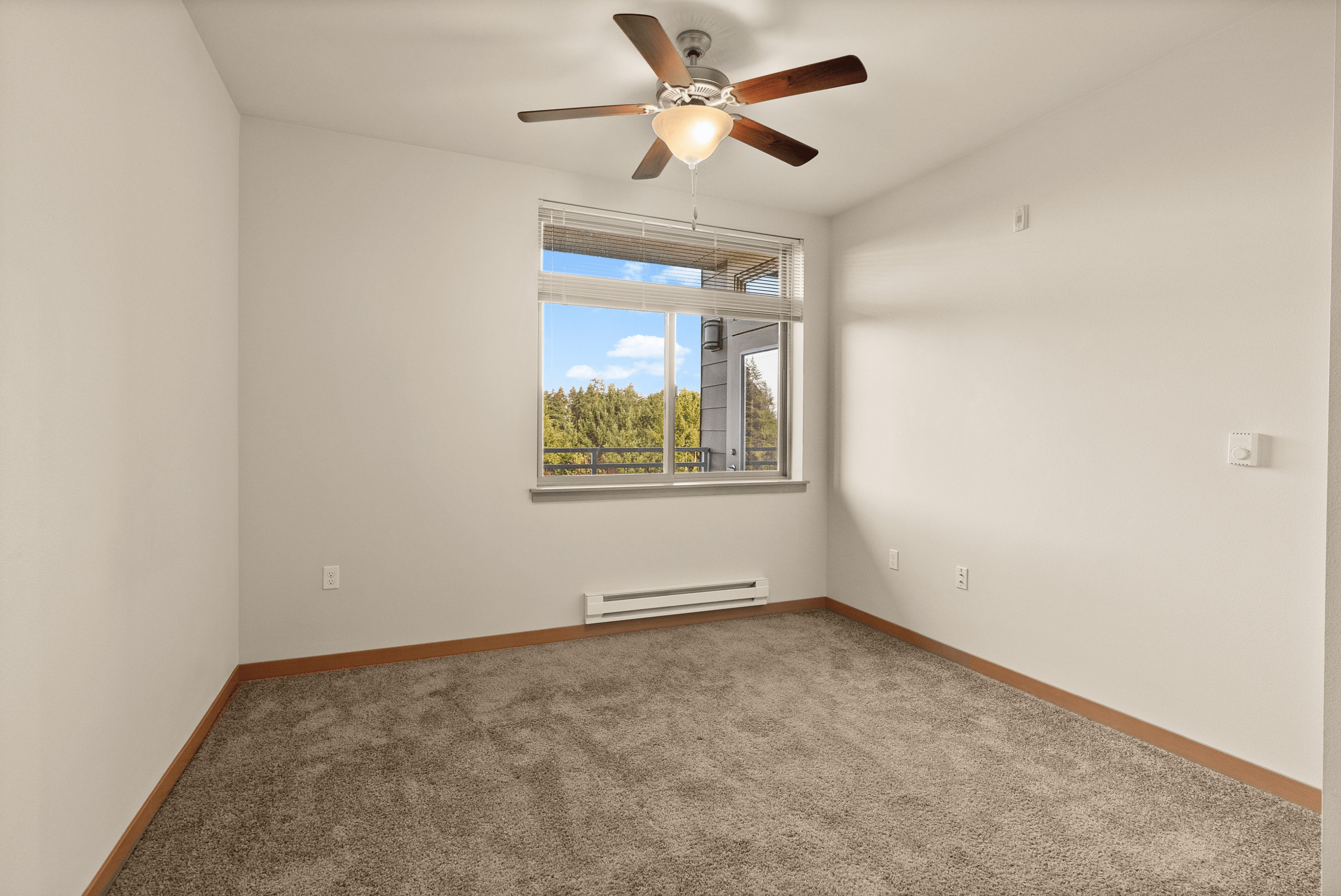 Bright bedroom with soft carpeting, large window offering a scenic view, and a modern ceiling fan.