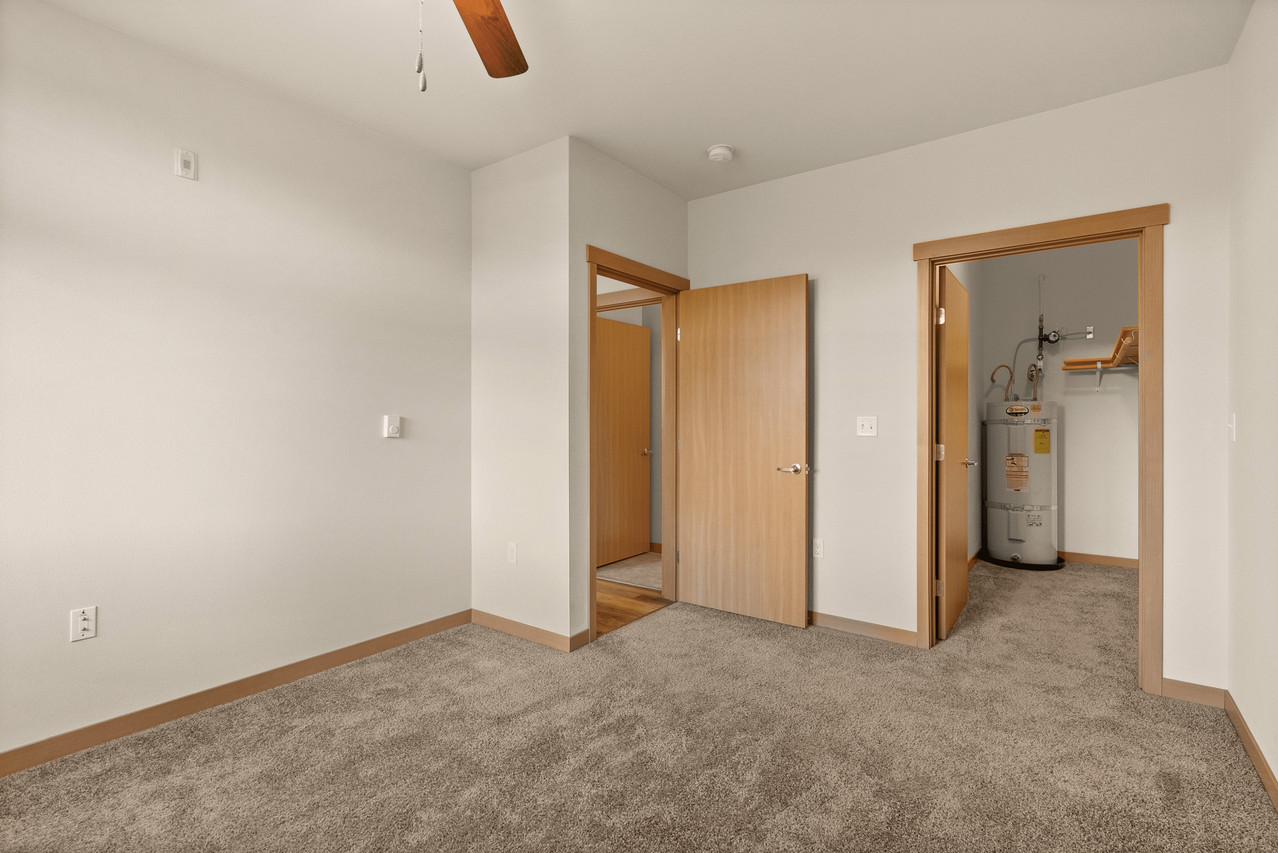 Cozy bedroom with carpeted floors, a ceiling fan, and a large window offering scenic views of trees.