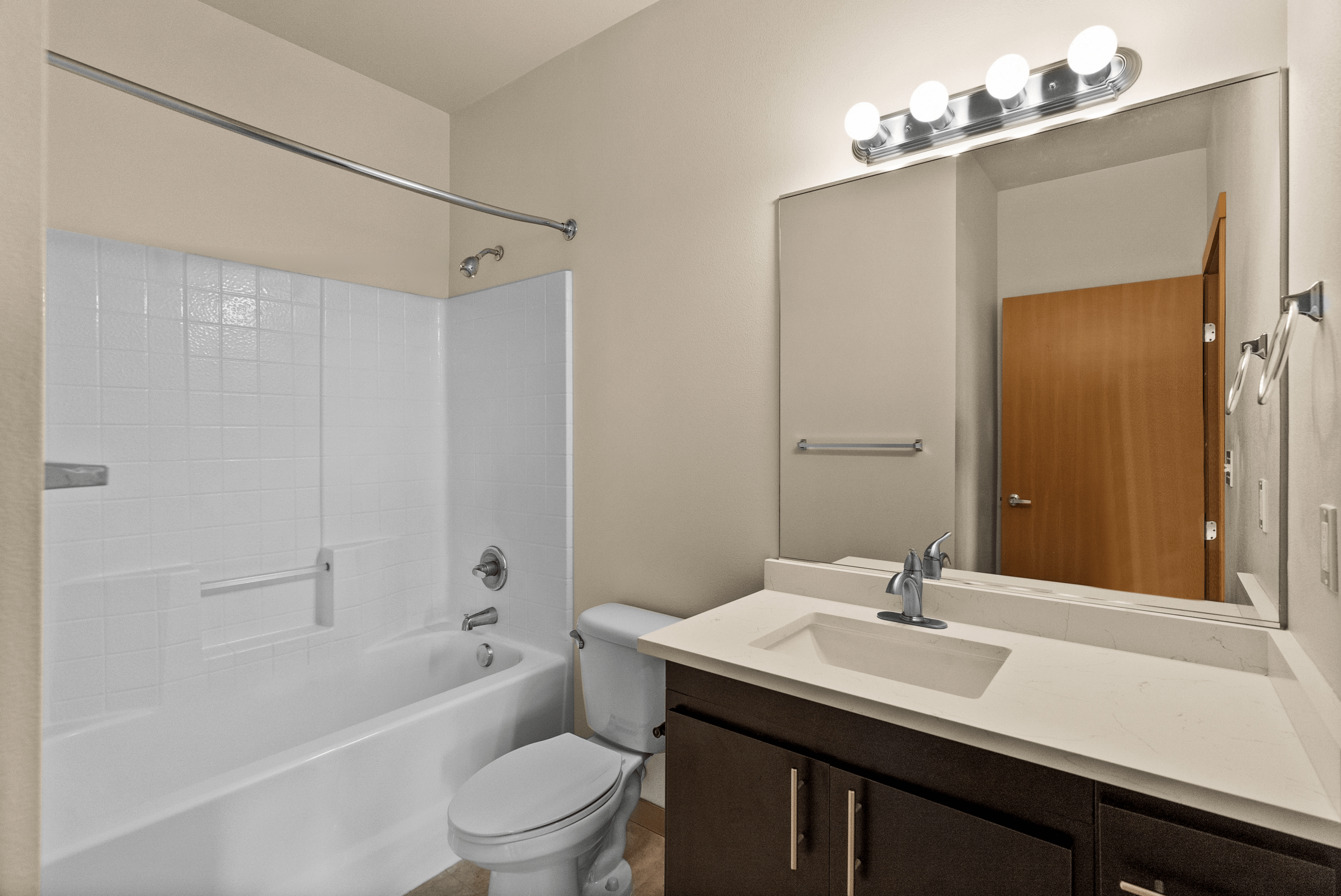 Modern bathroom featuring a sleek vanity with under-sink storage, bright lighting, and a clean bathtub with a curved shower rod.