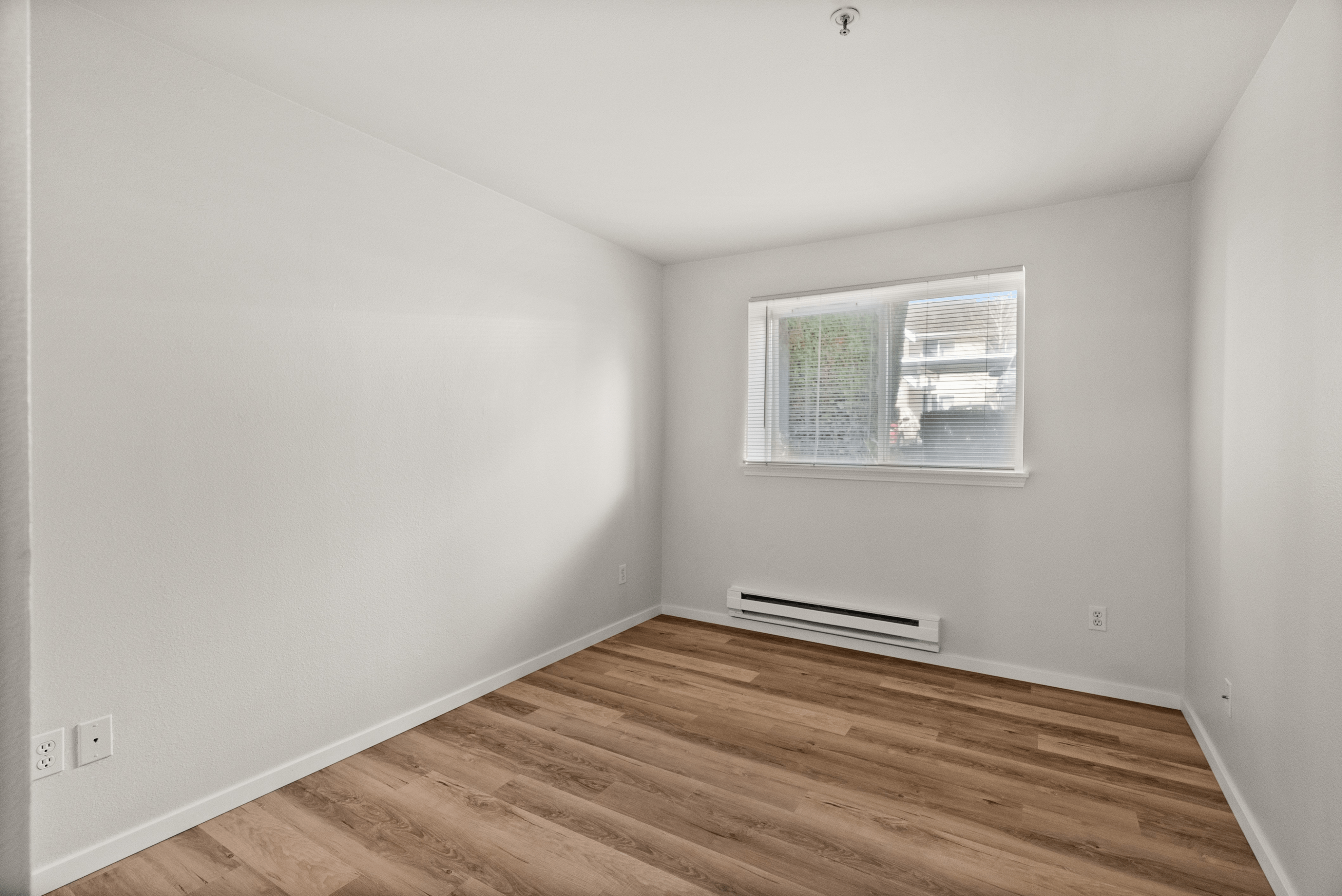 Bright, empty room with large window and wood flooring, ideal for a cozy bedroom or home office.