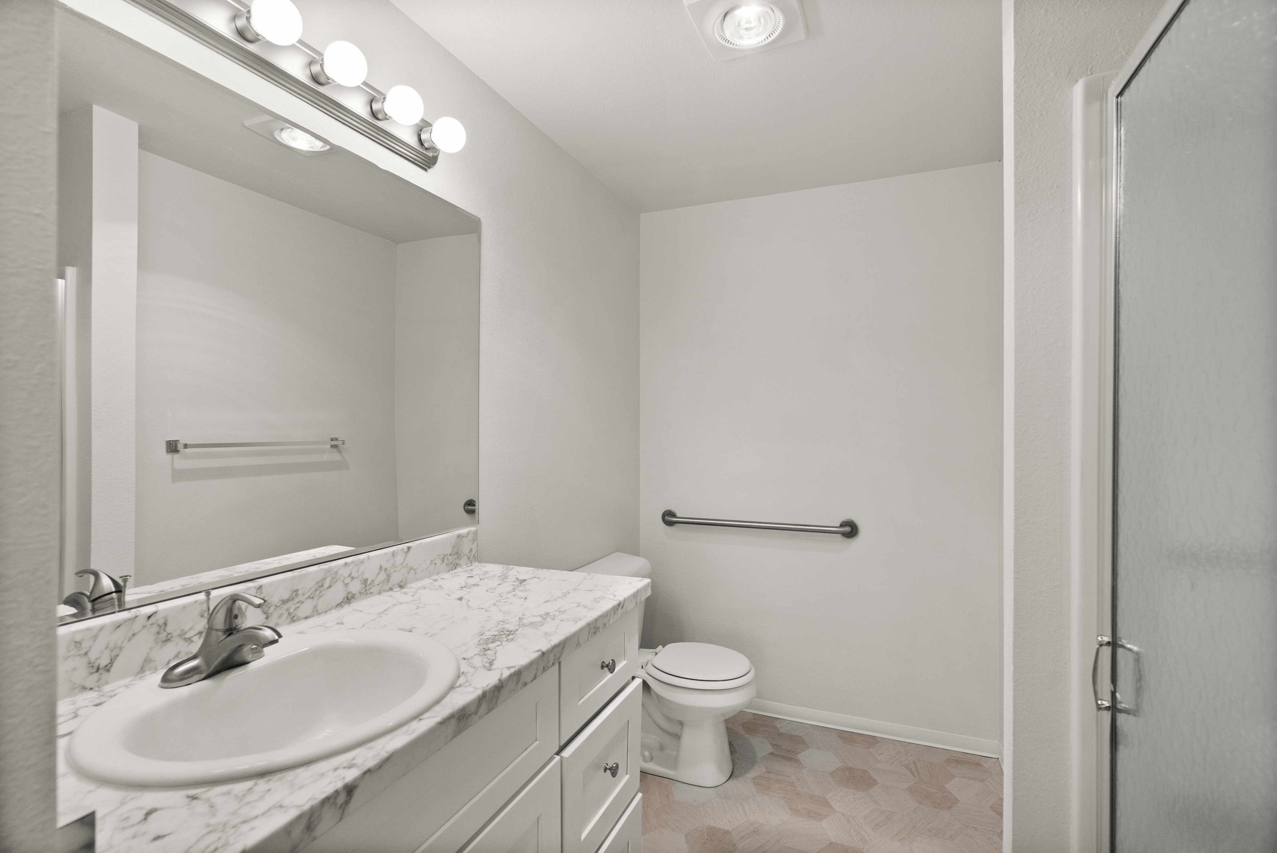 Modern bathroom with marble countertop, elegant lighting fixtures, and a sleek shower door, offering a luxurious touch.