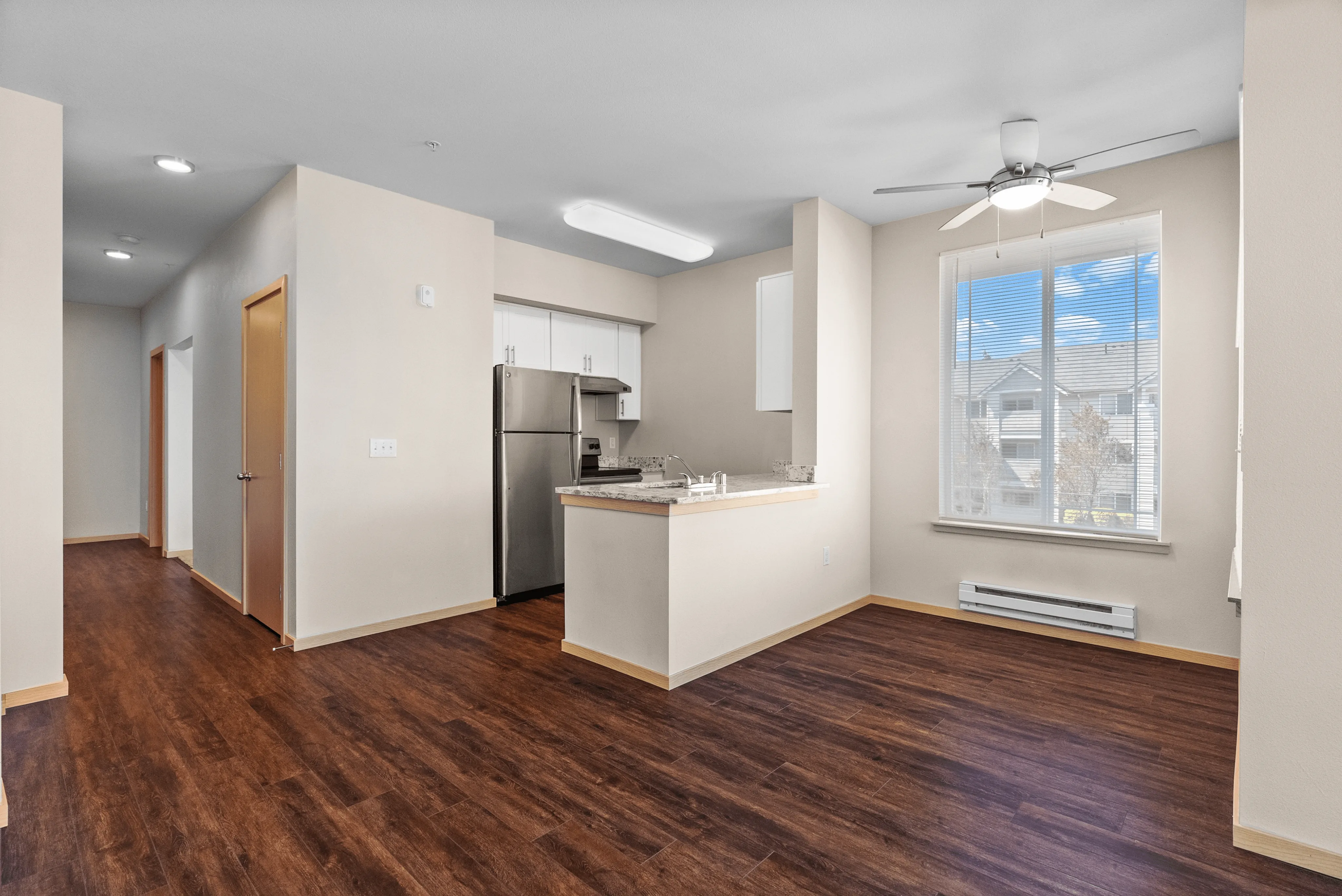Modern apartment kitchen with stainless steel appliances, wood-style flooring, and natural light from a large window in the dining nook.