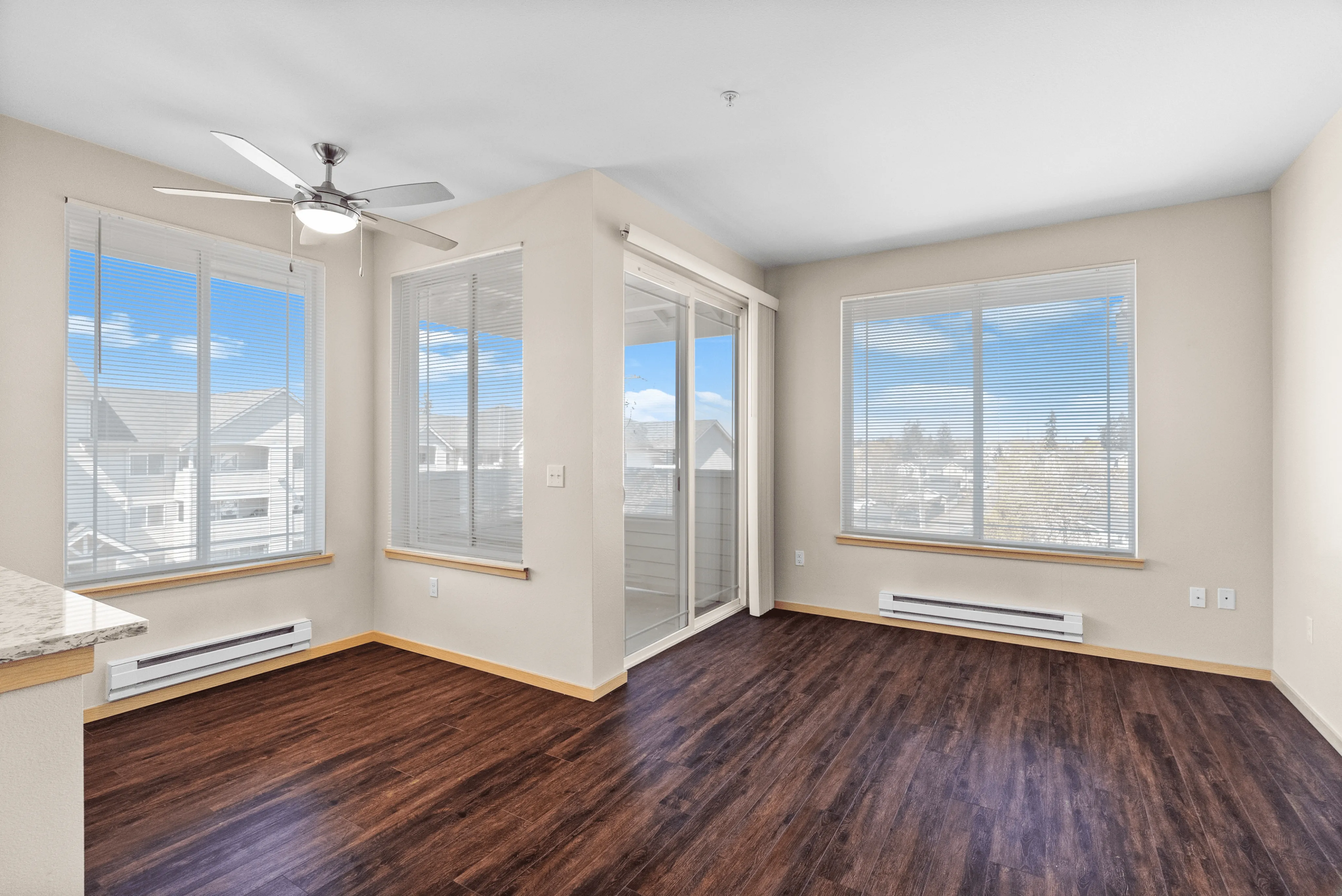 Bright living space with floor-to-ceiling windows, ceiling fan, wood-style flooring, and sliding glass doors leading to a private balcony.