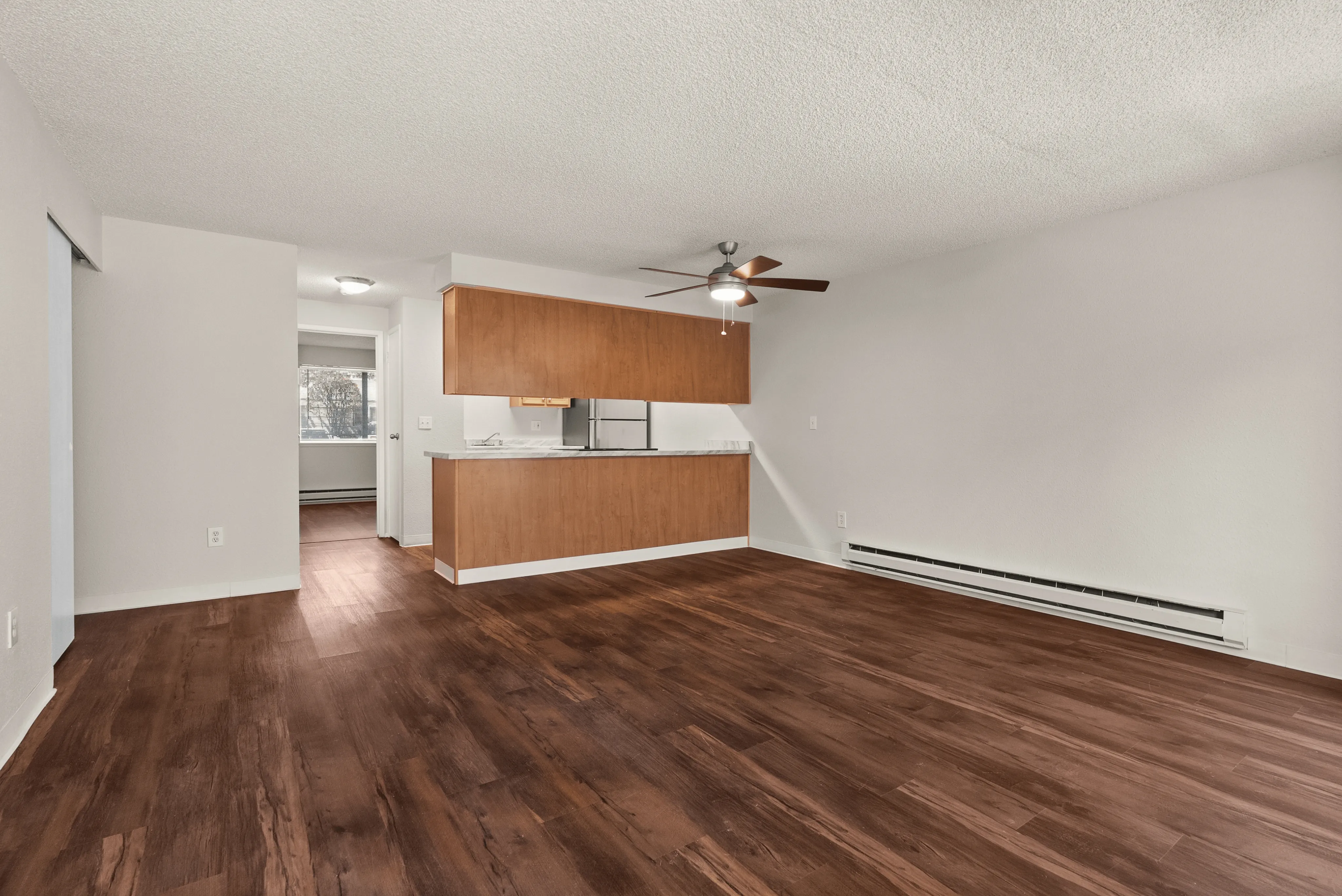Spacious open-plan living area with rich wooden floors, a modern kitchen featuring sleek cabinetry, and a ceiling fan for comfort.
