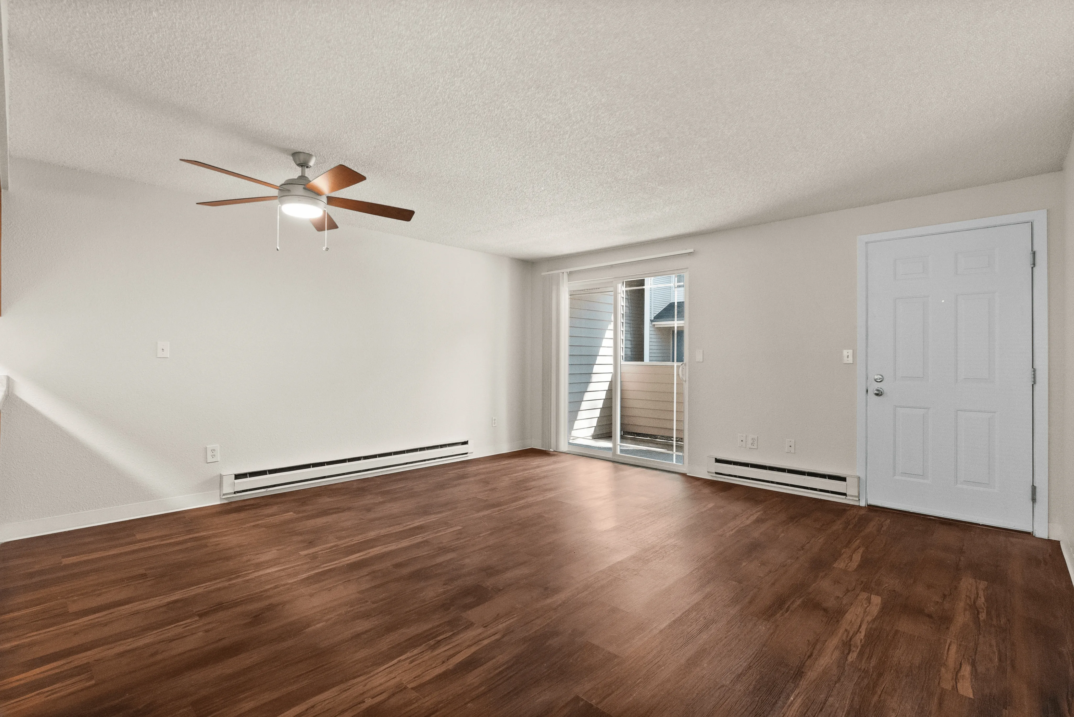 Spacious living room with elegant wood flooring and ceiling fan, enhanced by natural light through sliding glass doors.