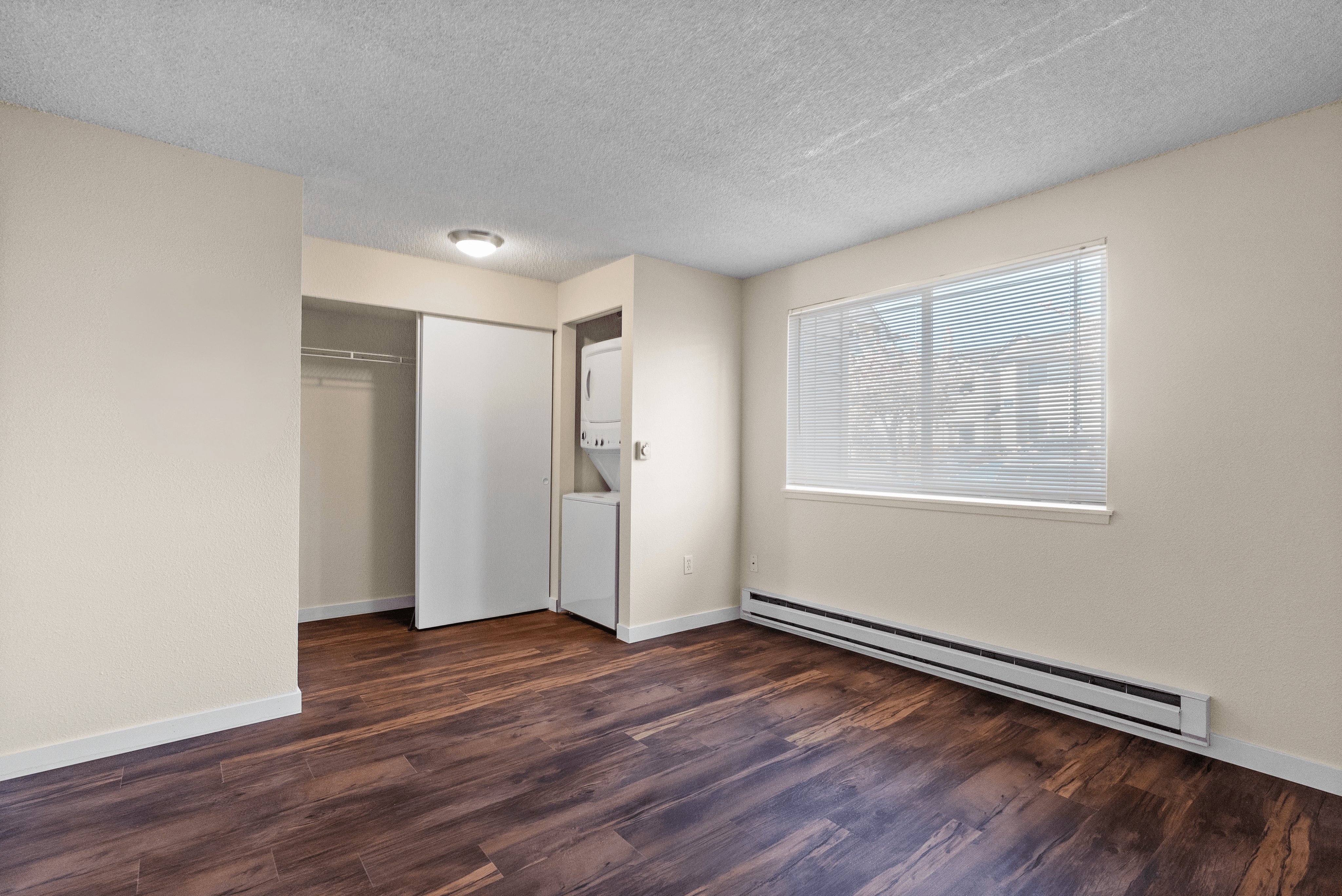 Inviting apartment interior featuring elegant wood flooring, large bright window, and in-unit laundry.
