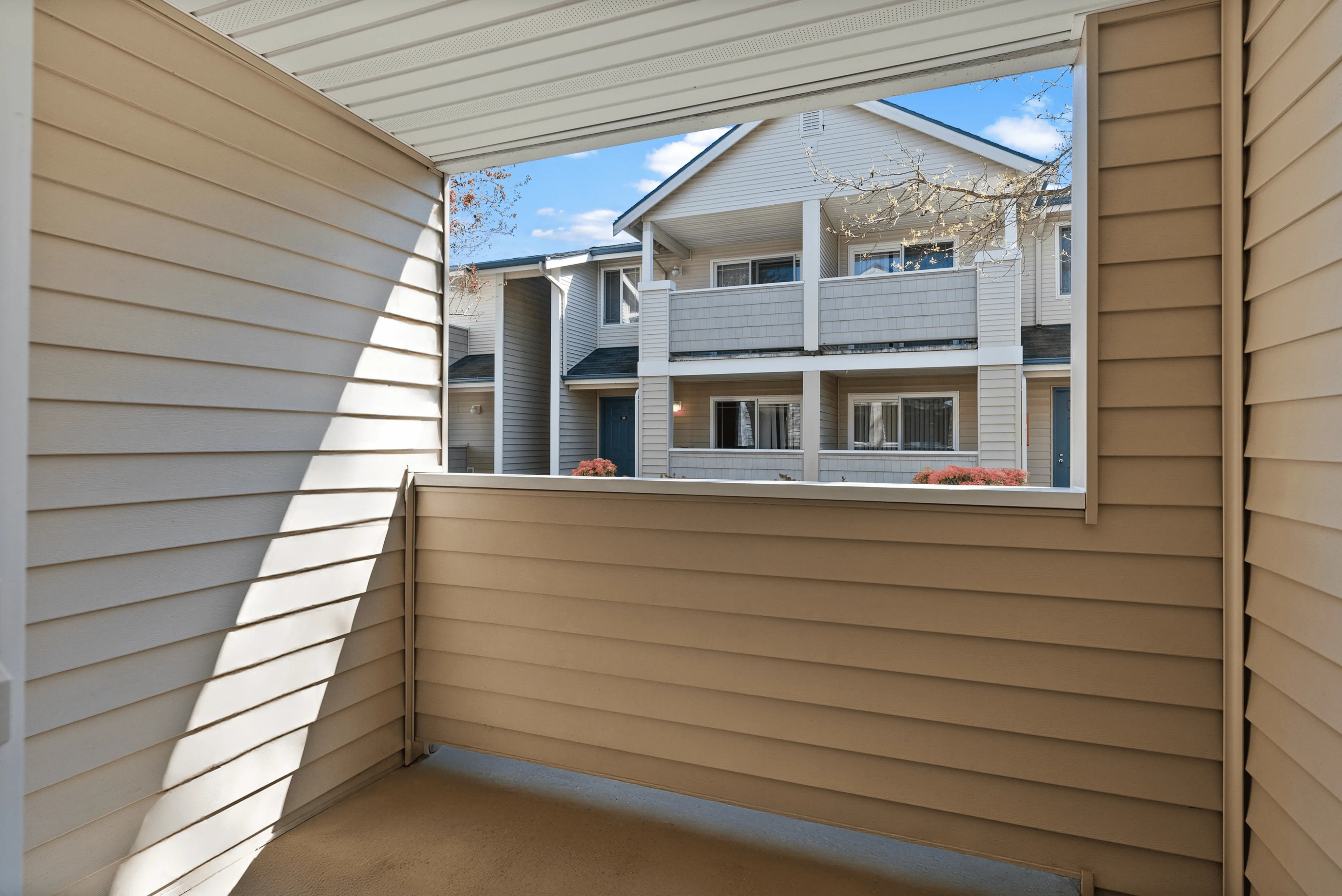 Private covered patio with beige siding and a view of neighboring apartment balconies in a well-maintained residential community.