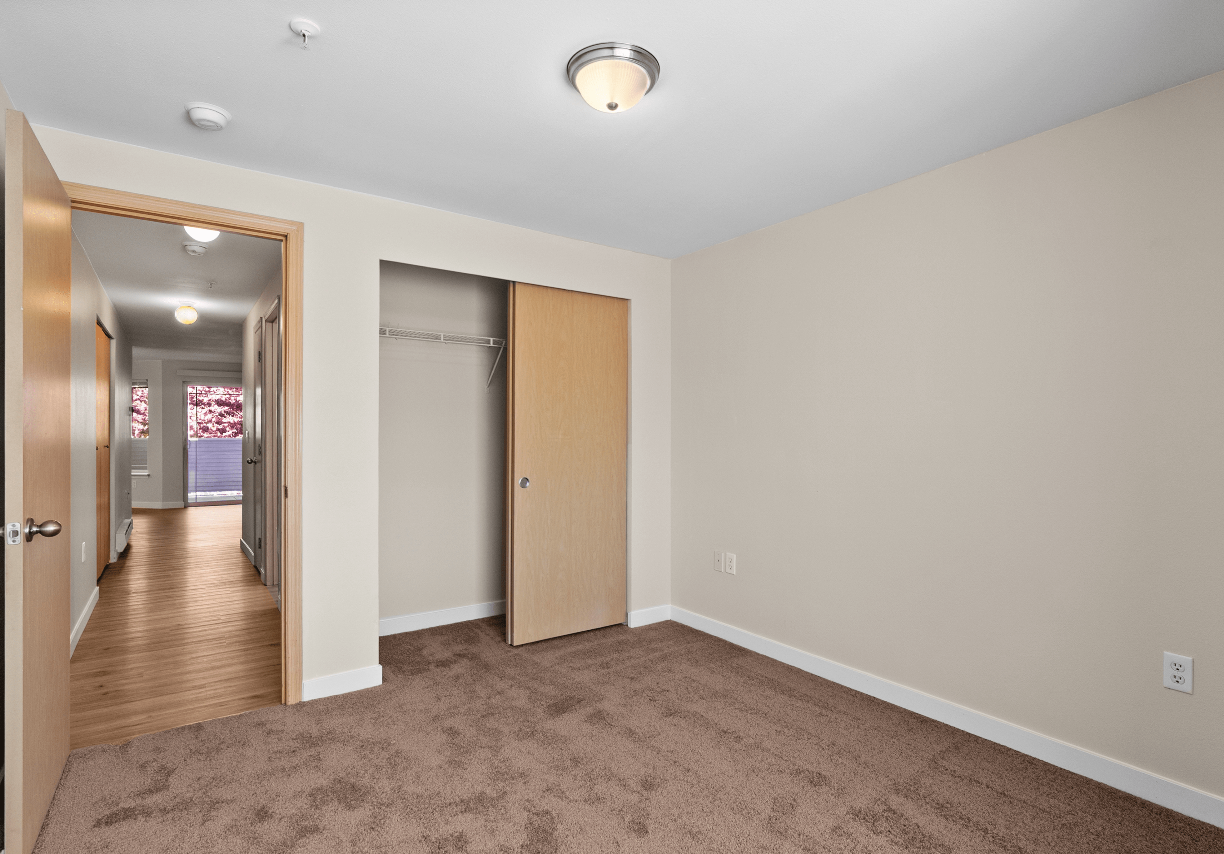 Inviting bedroom with plush carpet, ample closet space, and a view of a bright hallway leading to a balcony.