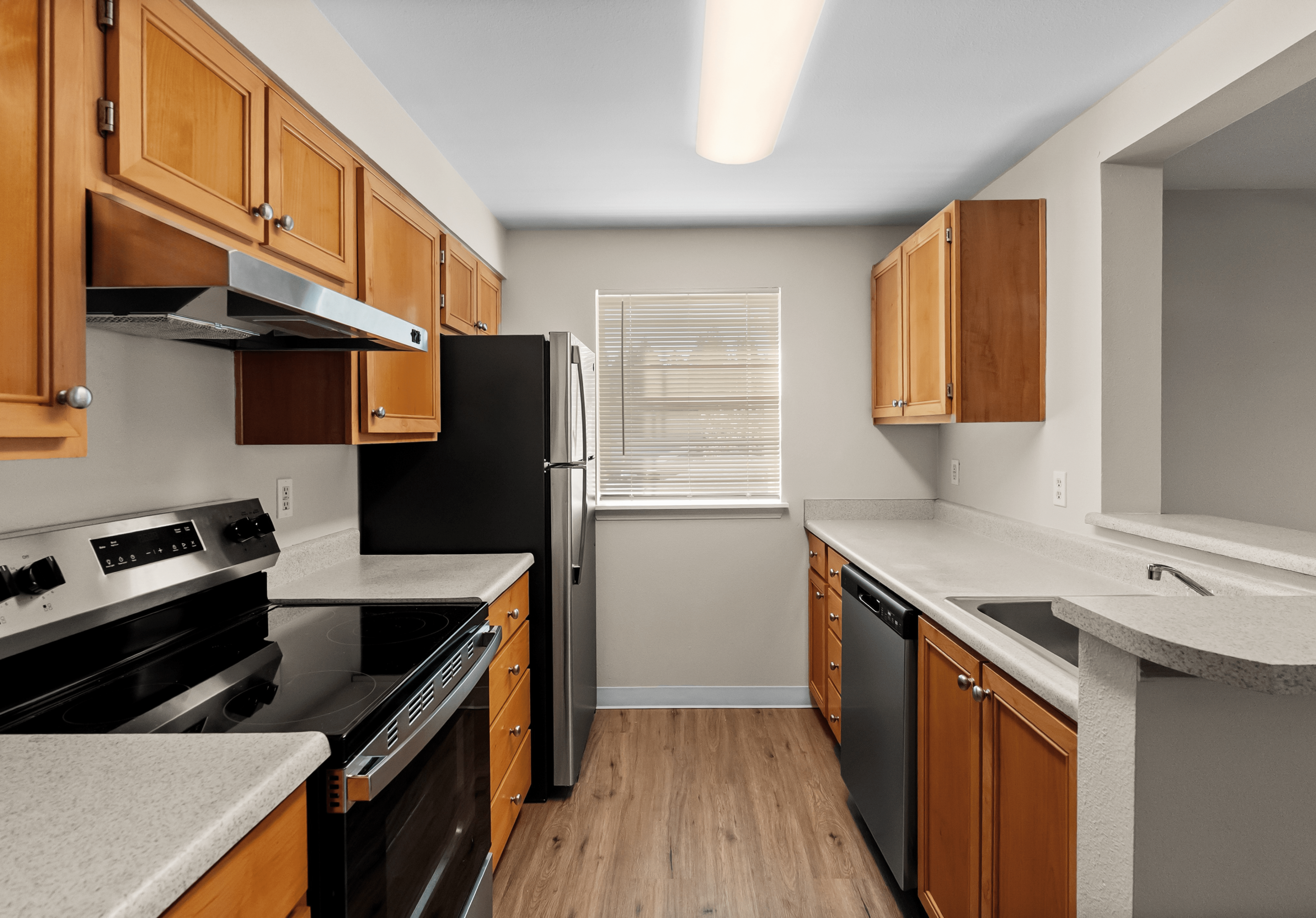 Bright and modern kitchen with hardwood floors, sleek stainless steel appliances, and ample wood cabinetry.