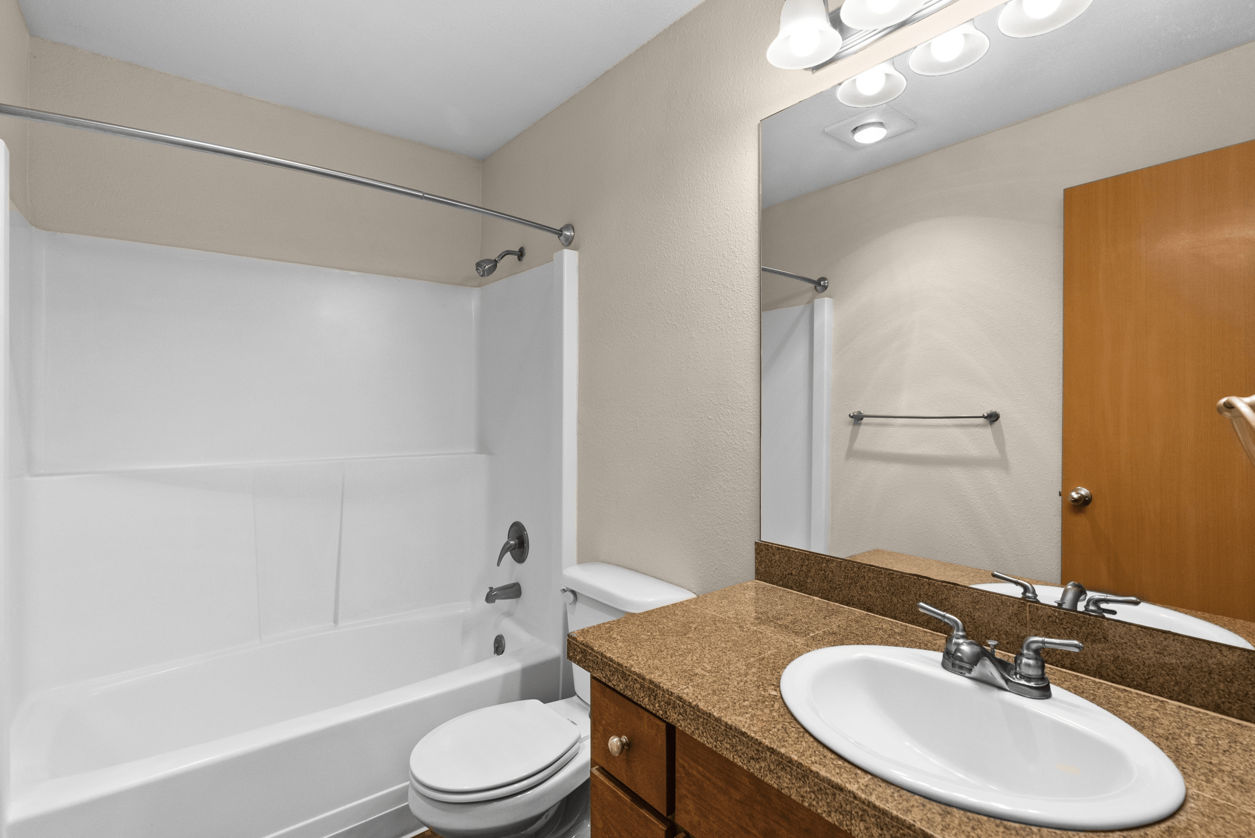 Modern bathroom featuring a sleek vanity with a granite countertop, large mirror, and a pristine bathtub with a shower.