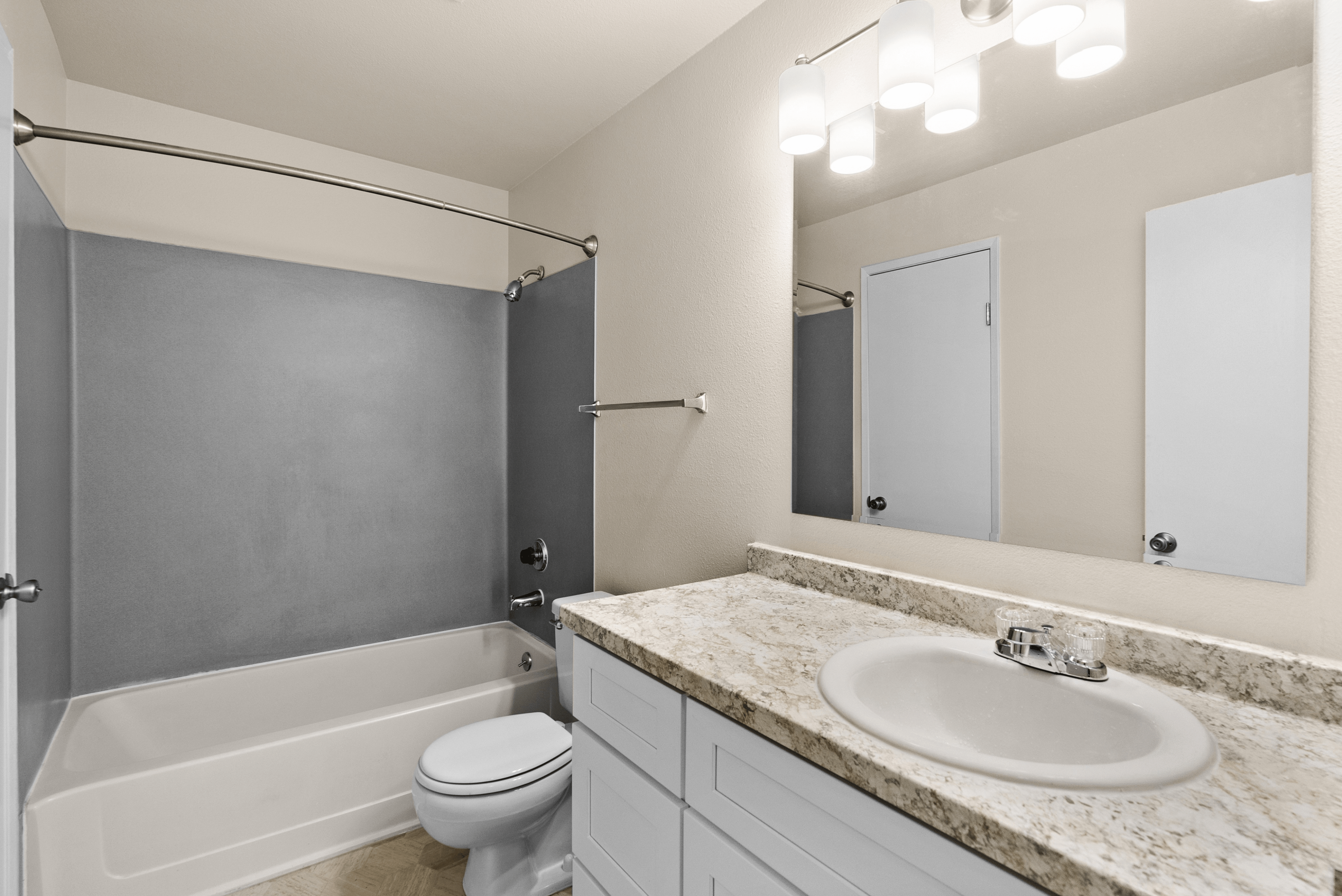 Modern bathroom with elegant granite countertop, spacious mirror, and contemporary lighting.