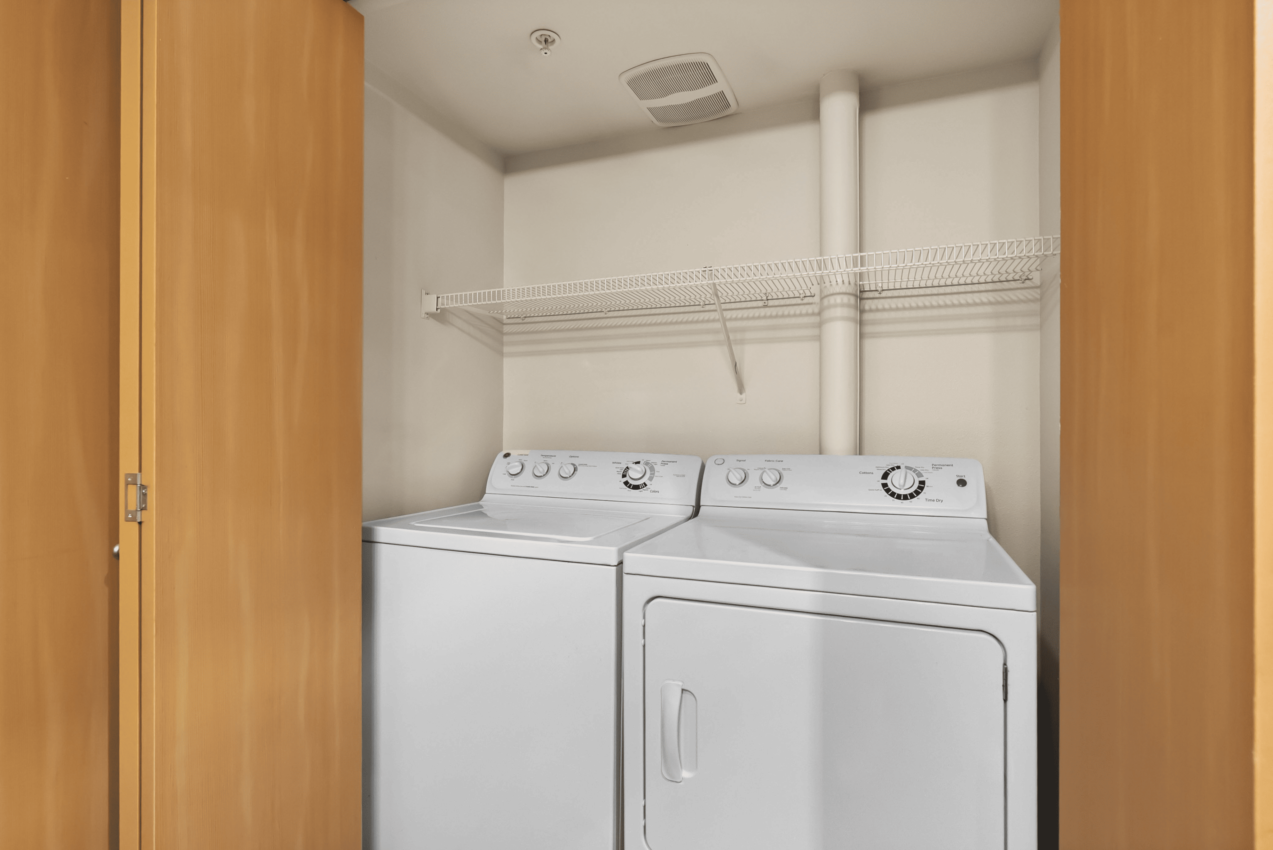 Convenient in-unit laundry space with modern washer and dryer, enclosed by sleek wooden doors.