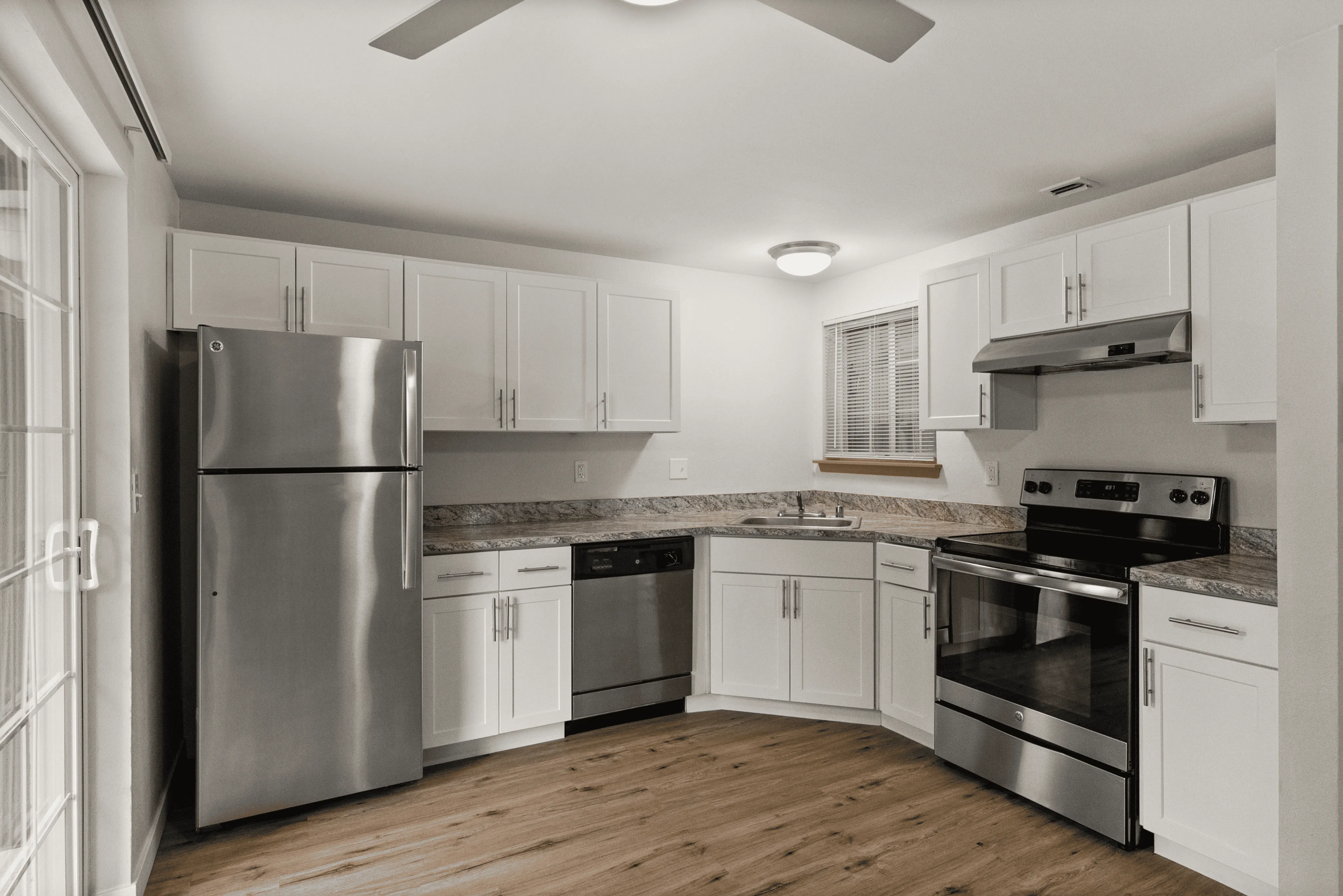Contemporary kitchen with stainless steel appliances, white cabinets, and wood flooring.