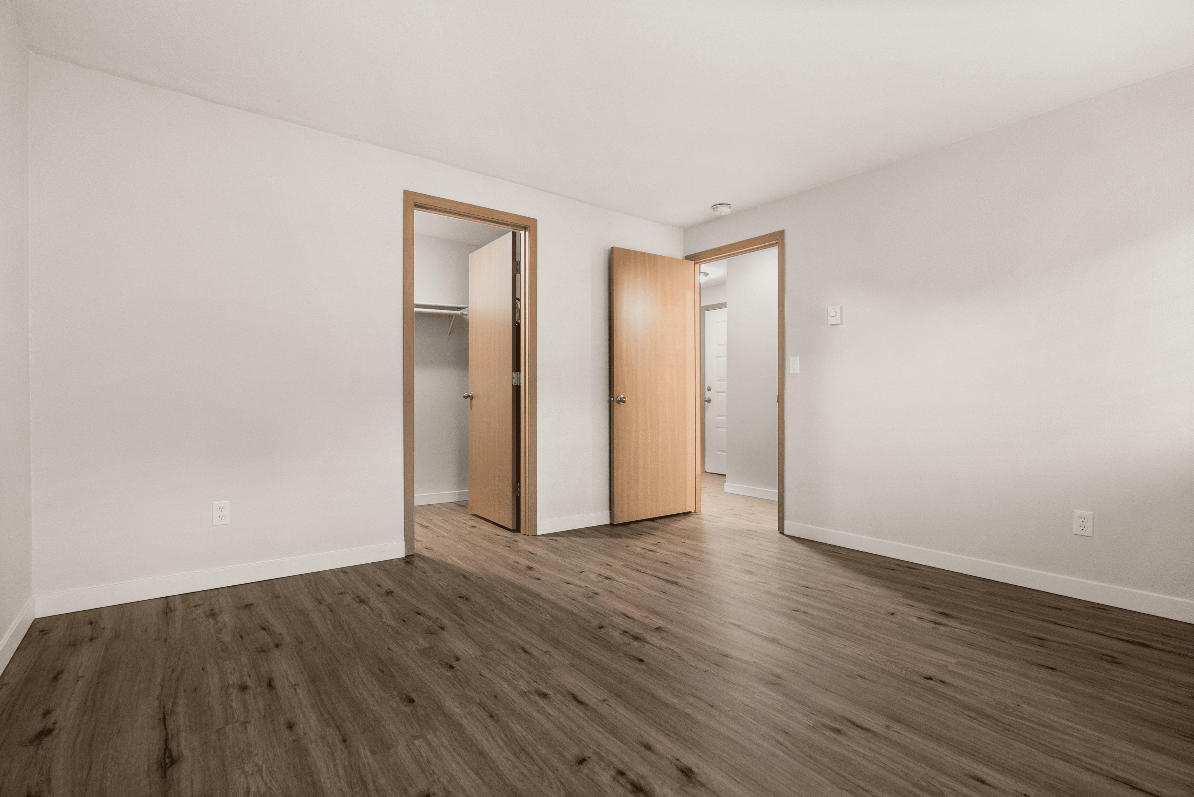 Spacious bedroom featuring elegant hardwood flooring, modern wooden doors, and a roomy closet area.