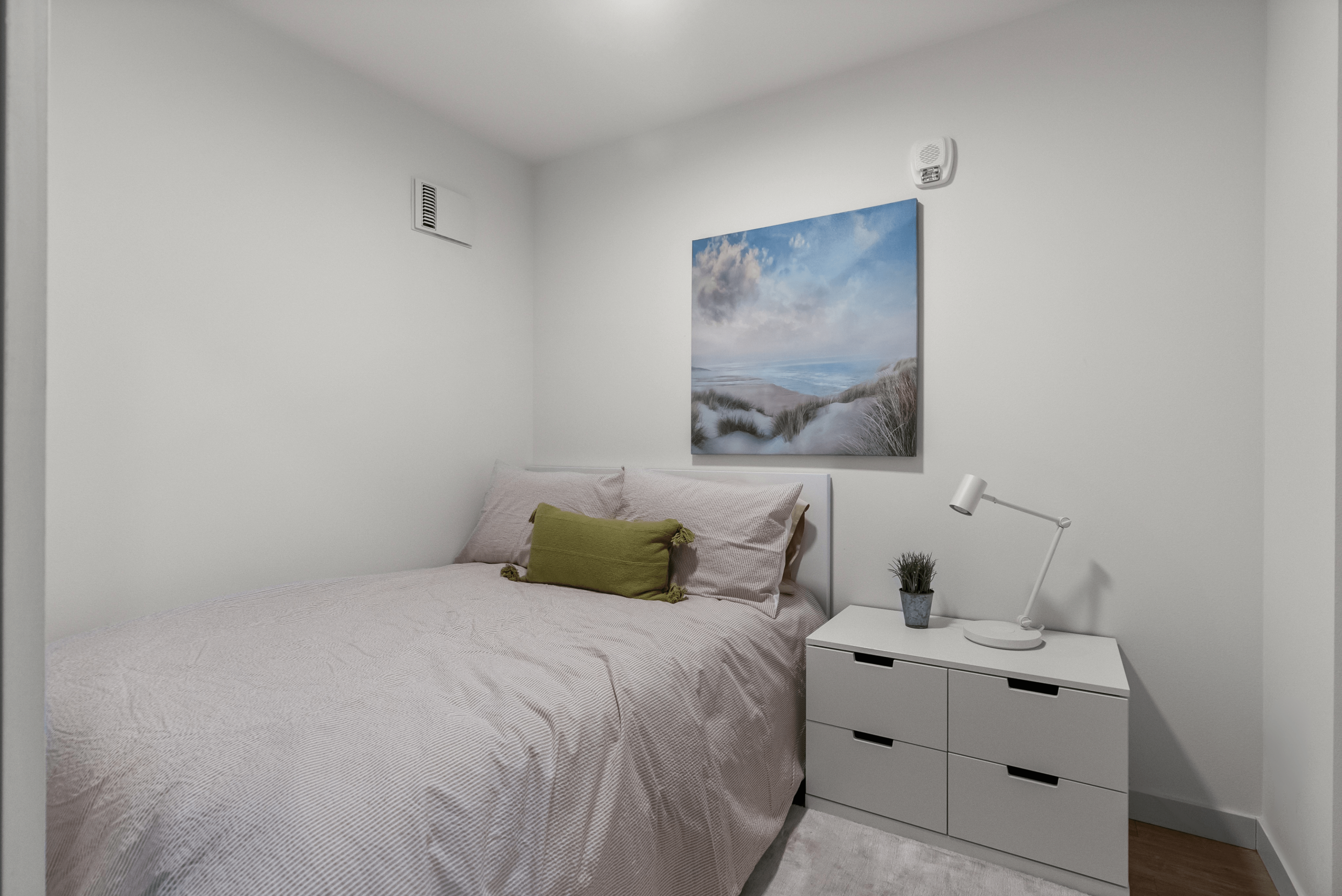 Cozy bedroom with a plush bed, ocean-themed artwork, and sleek modern nightstand.