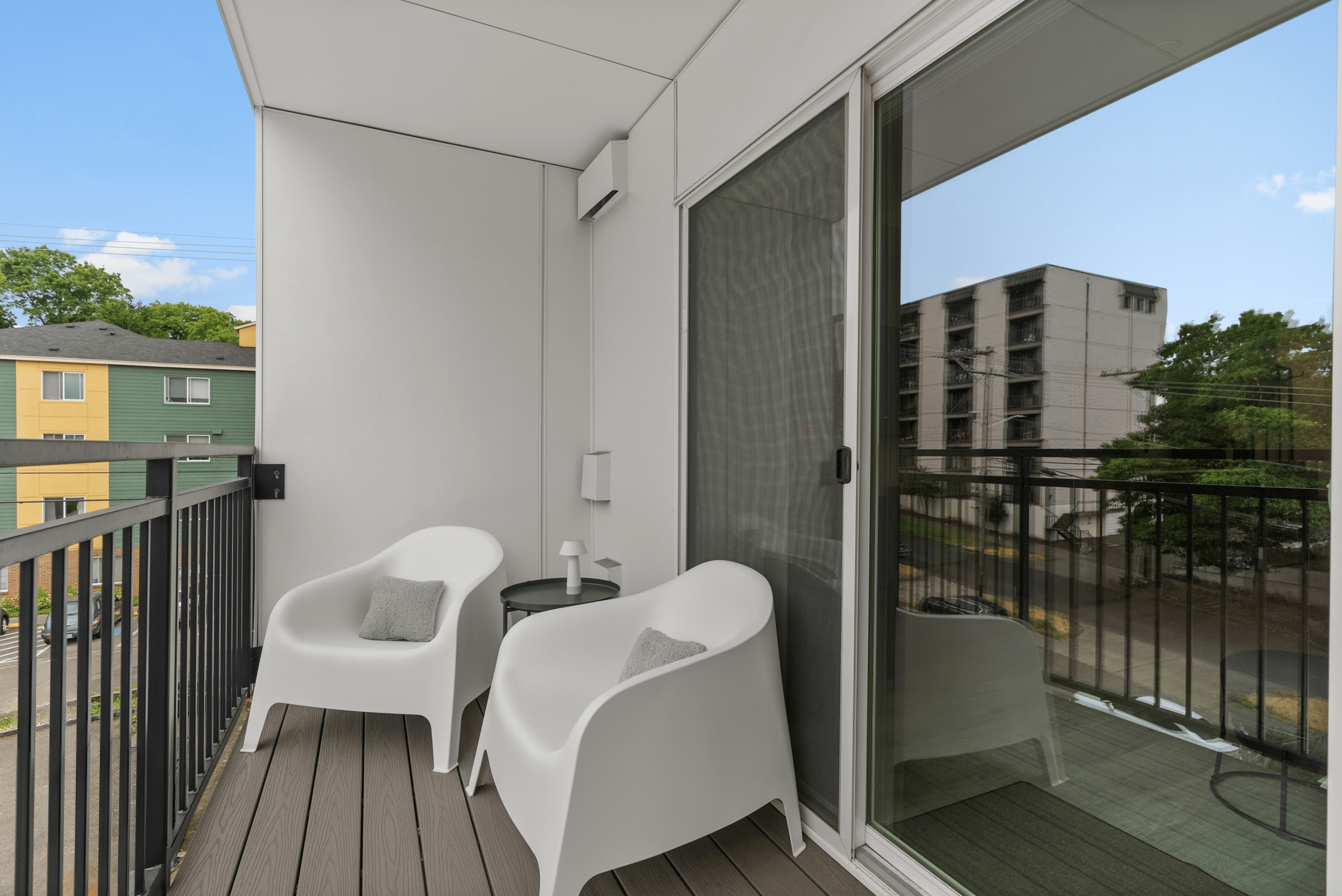 Modern balcony space with sleek white chairs, a cozy table, and scenic neighborhood views, perfect for relaxation.
