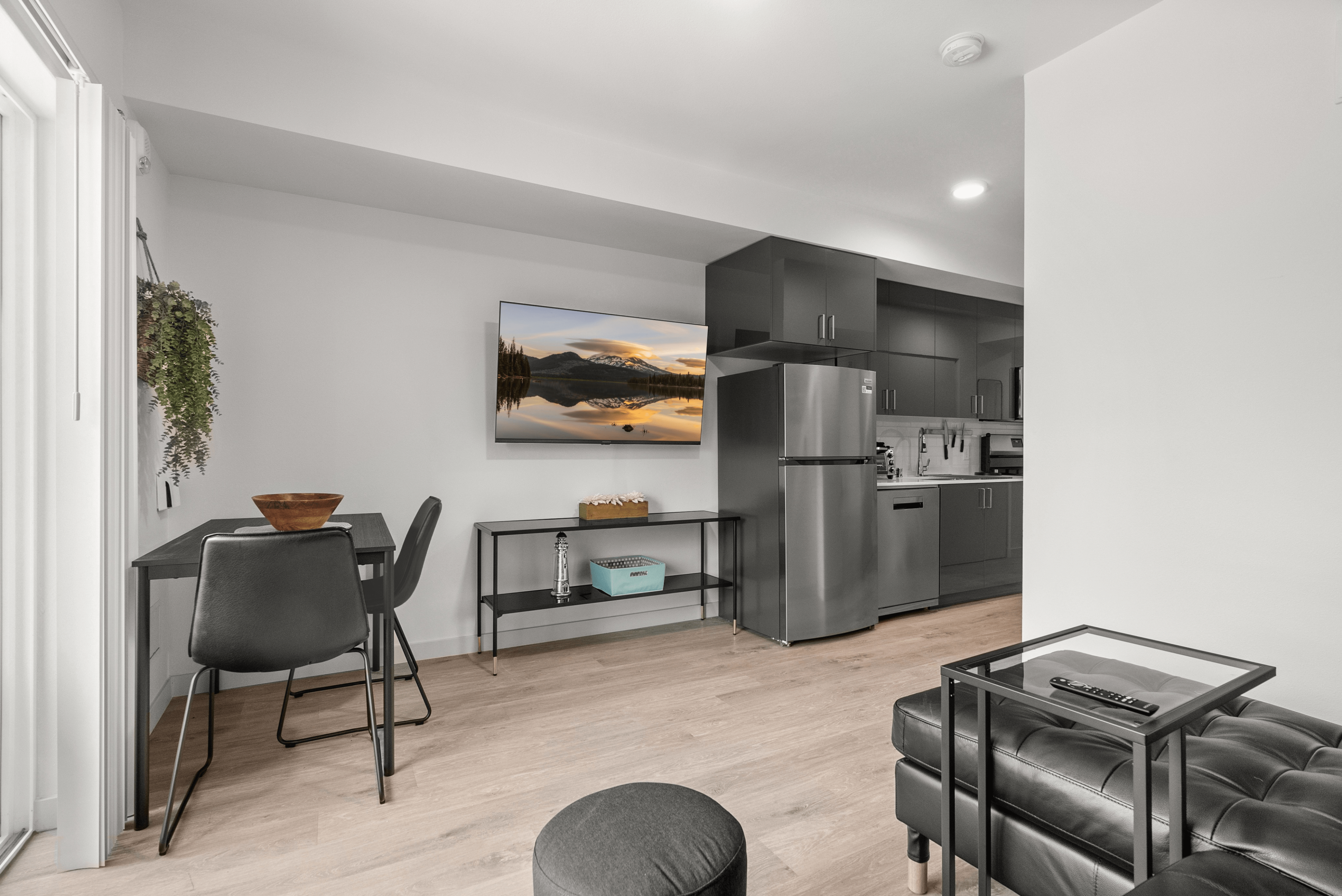 Modern open-concept kitchen and dining area with sleek stainless steel appliances and stylish black furnishings, featuring a wall-mounted TV and contemporary decor.