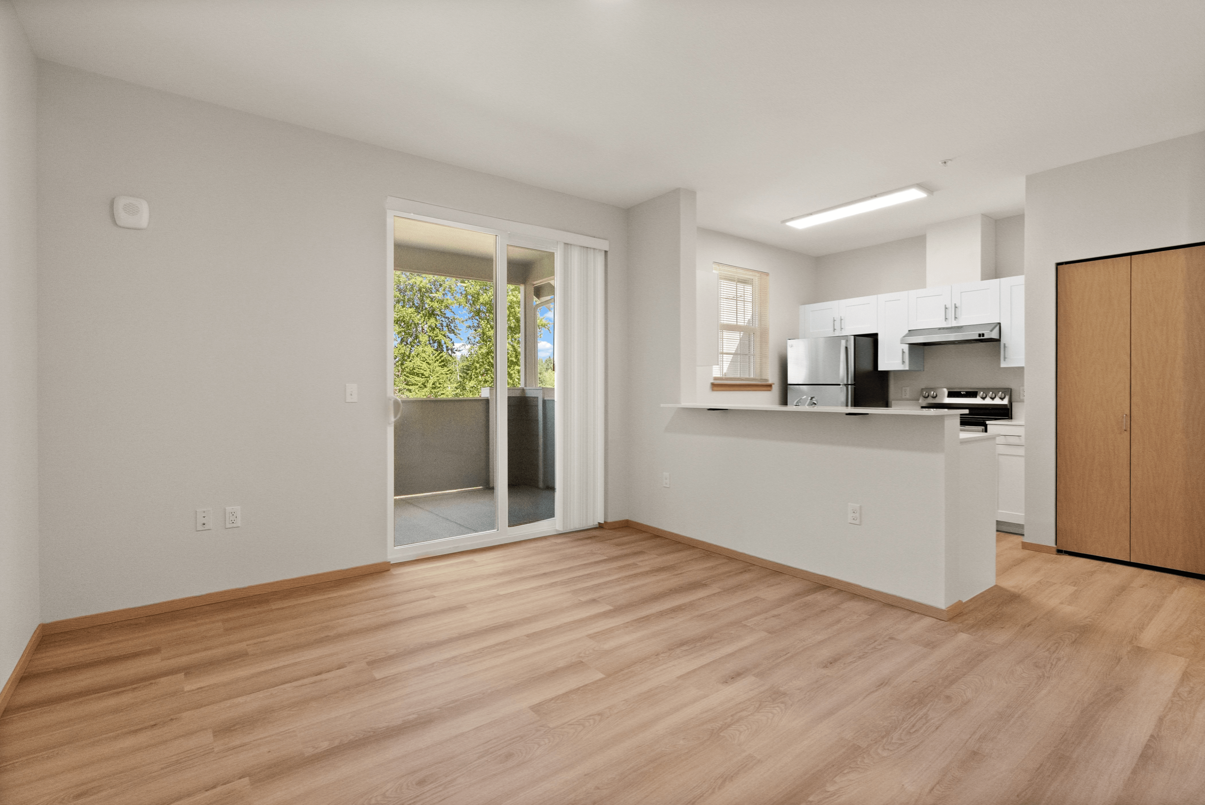 Bright open-concept living space with modern kitchen, sleek appliances, and sliding glass doors leading to a balcony with green views.