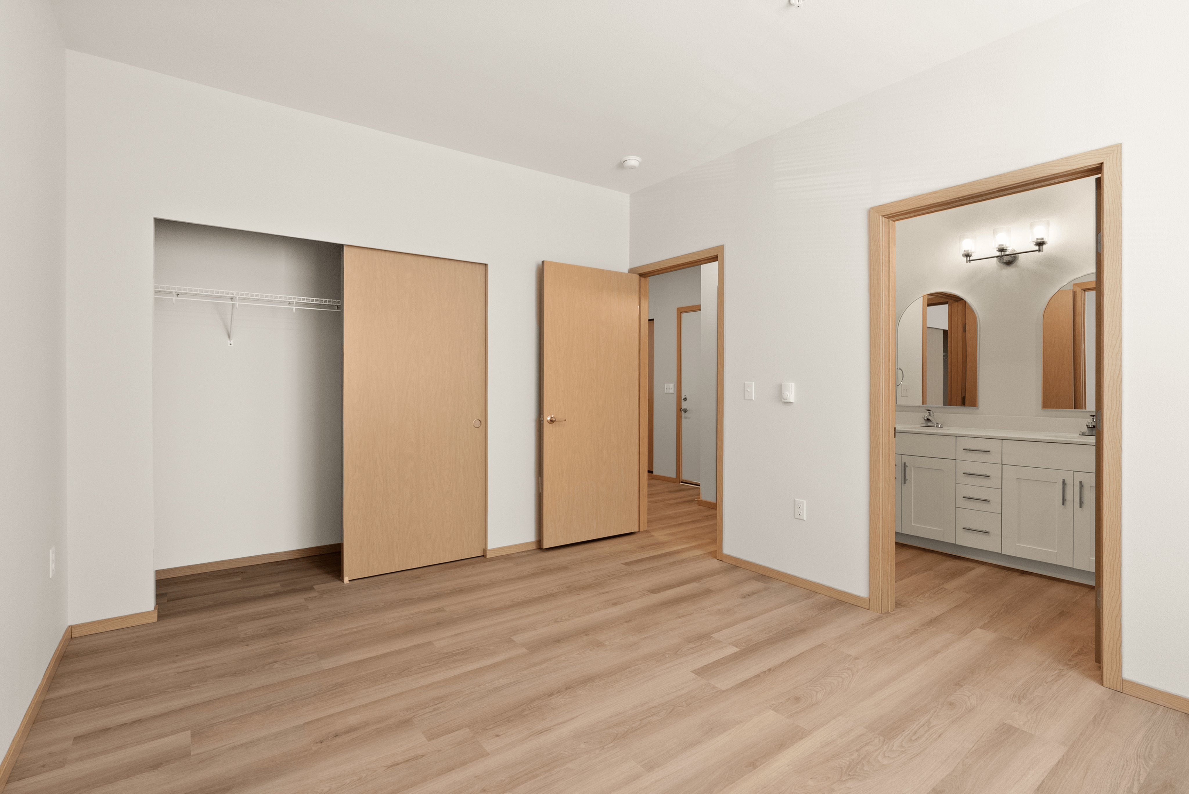 Modern bedroom with sleek wooden flooring, spacious closet, and ensuite bathroom featuring elegant lighting.