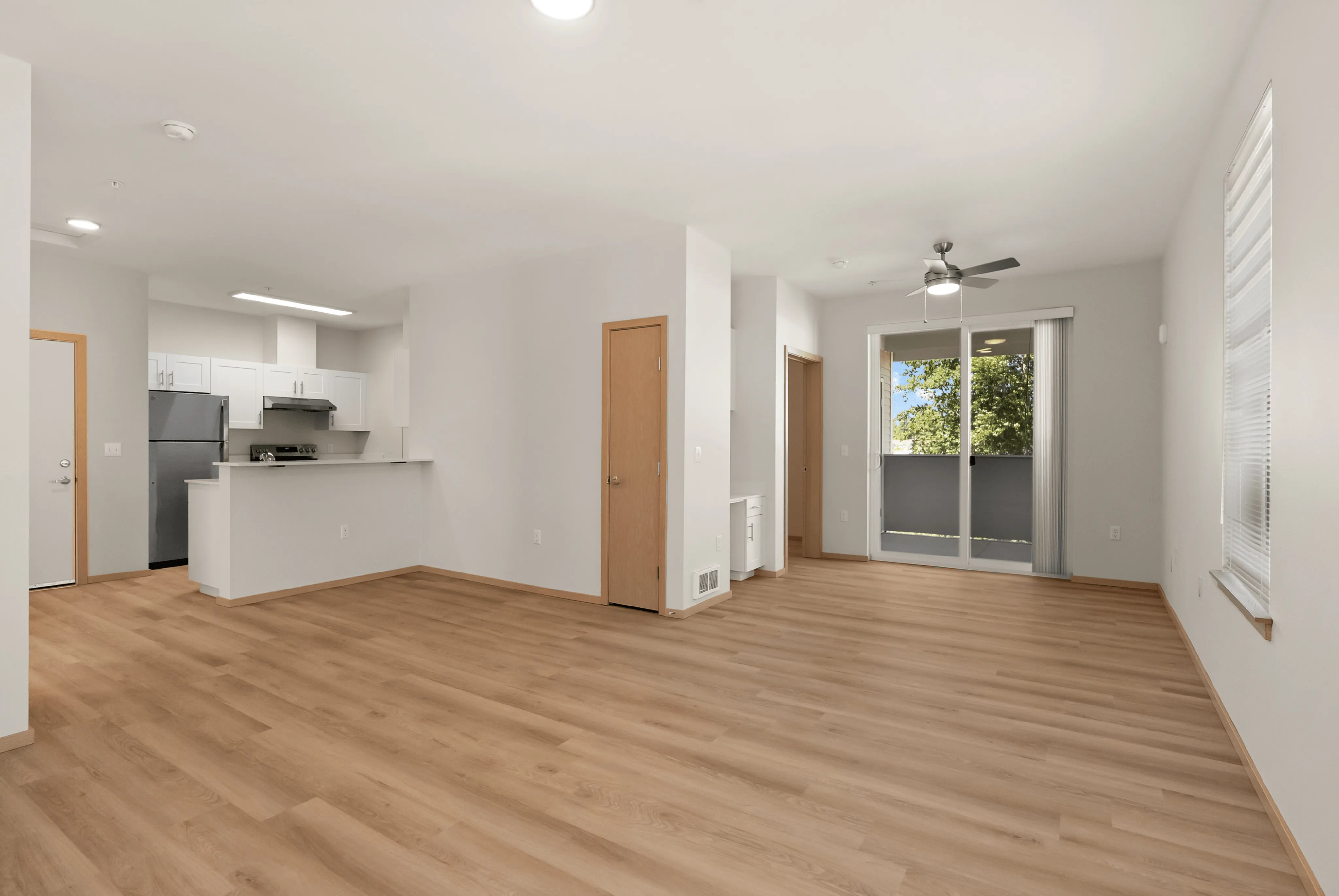 Bright and spacious open-concept living area featuring elegant hardwood flooring, a modern kitchen with stainless steel appliances, and sliding glass doors leading to a scenic balcony view.