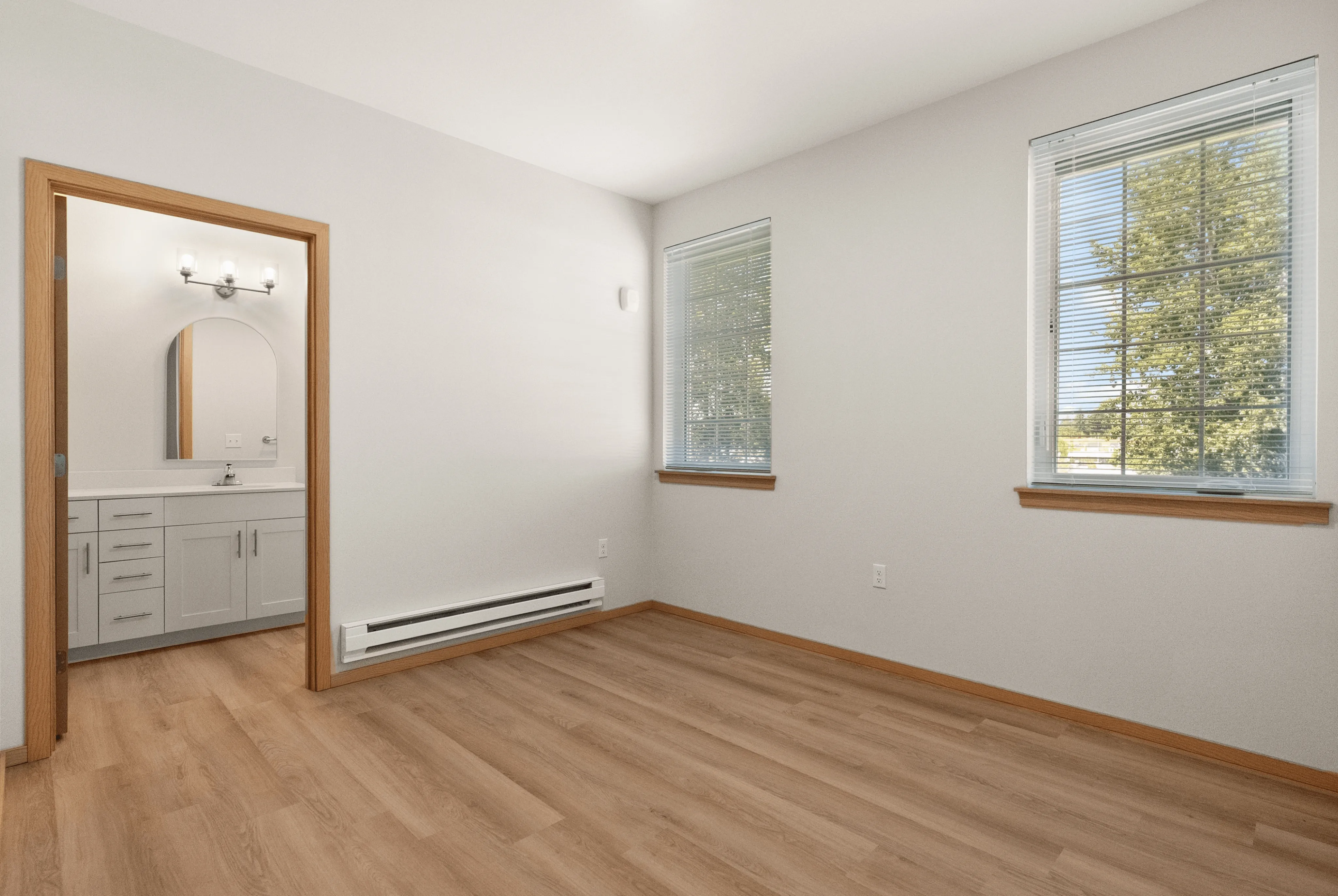 Bright and inviting bedroom with hardwood floors and two large windows, featuring an elegant ensuite bathroom.