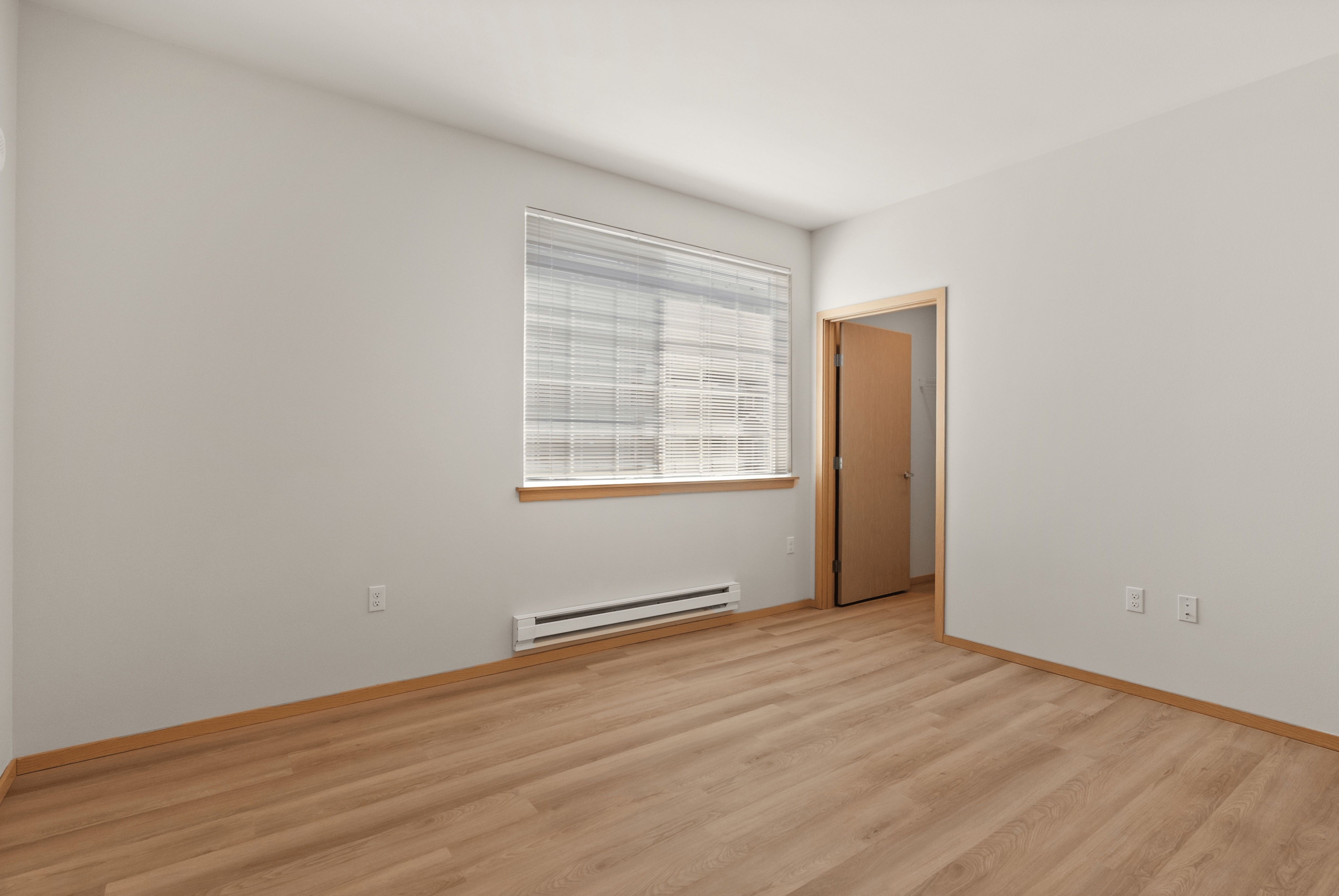 Bright bedroom with hardwood floors, natural light from a large window, and a wooden door leading to the closet.
