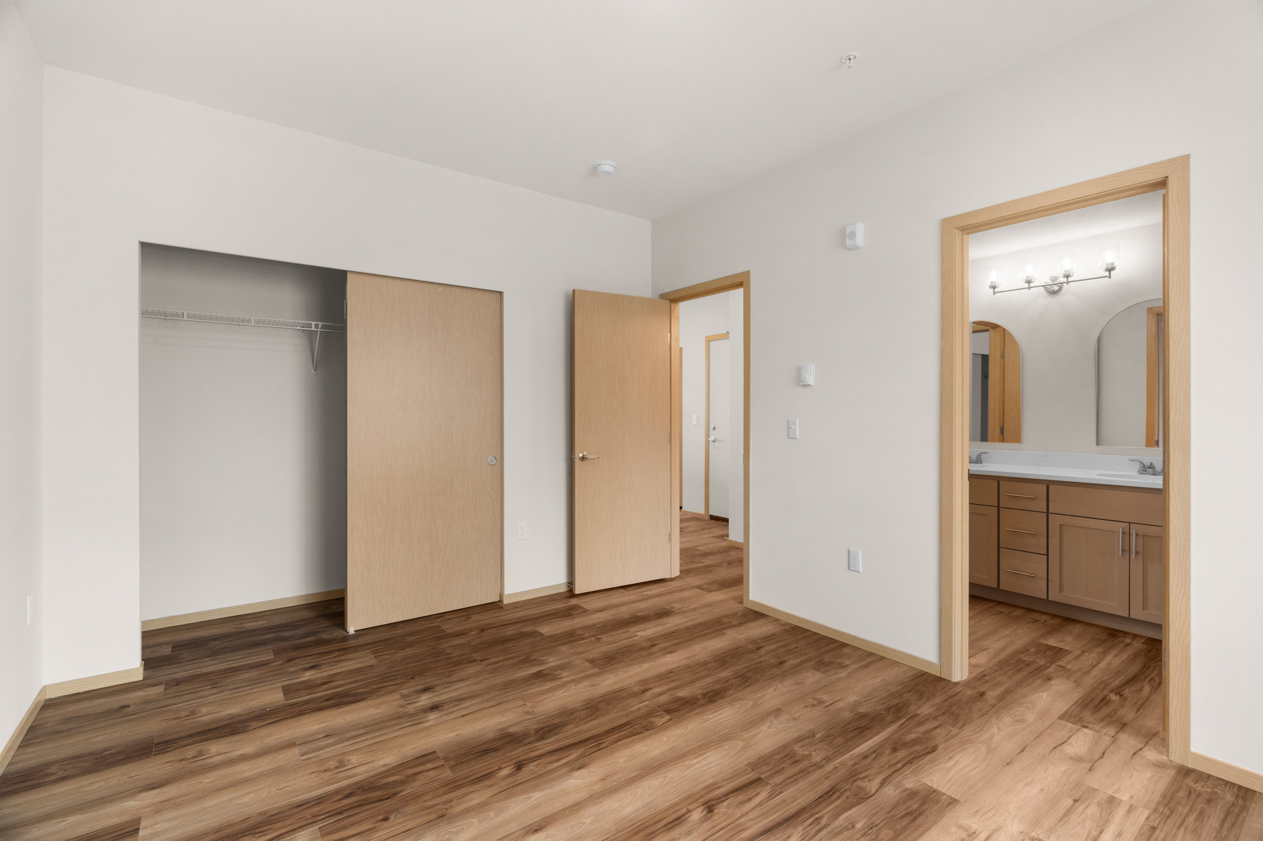 Inviting bedroom with warm wood flooring, spacious closet, and ensuite bathroom featuring modern fixtures and ample storage.
