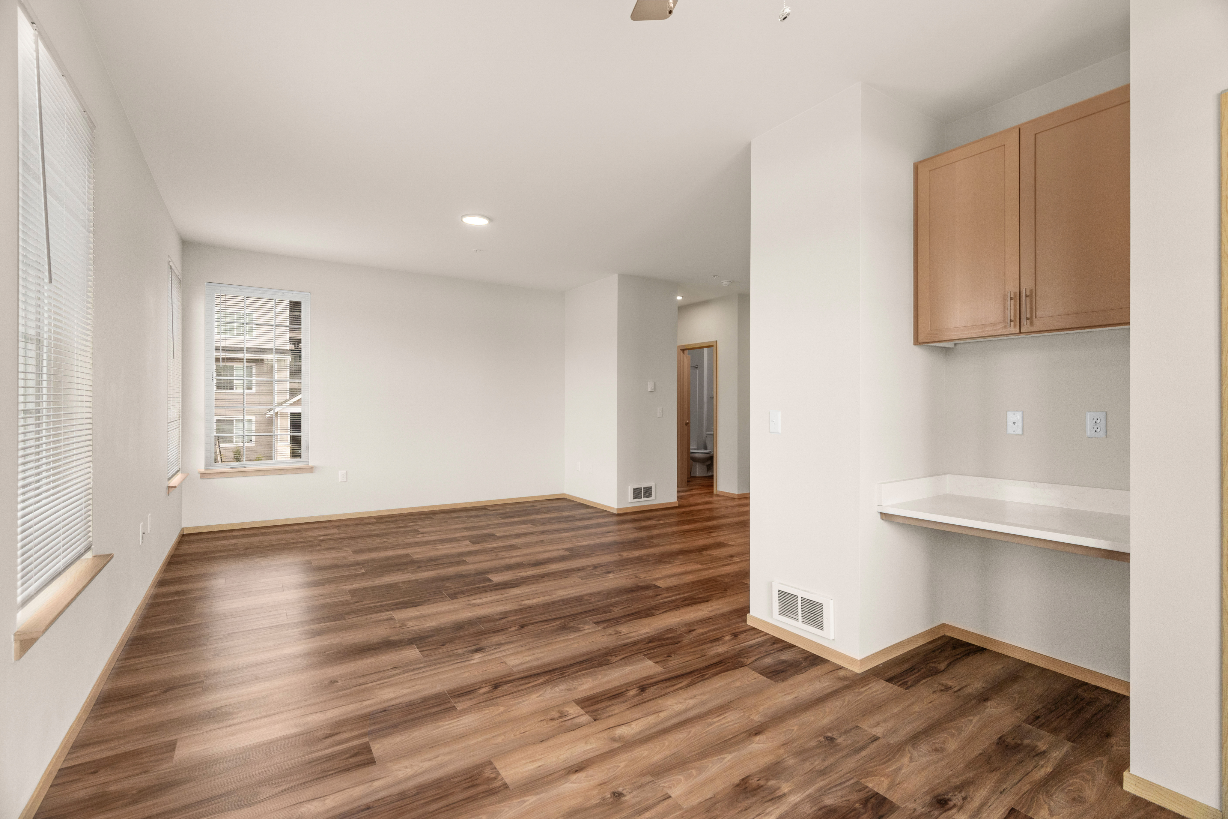 Spacious and bright living area with elegant wooden flooring, large windows for natural light, and a cozy nook with built-in cabinetry.