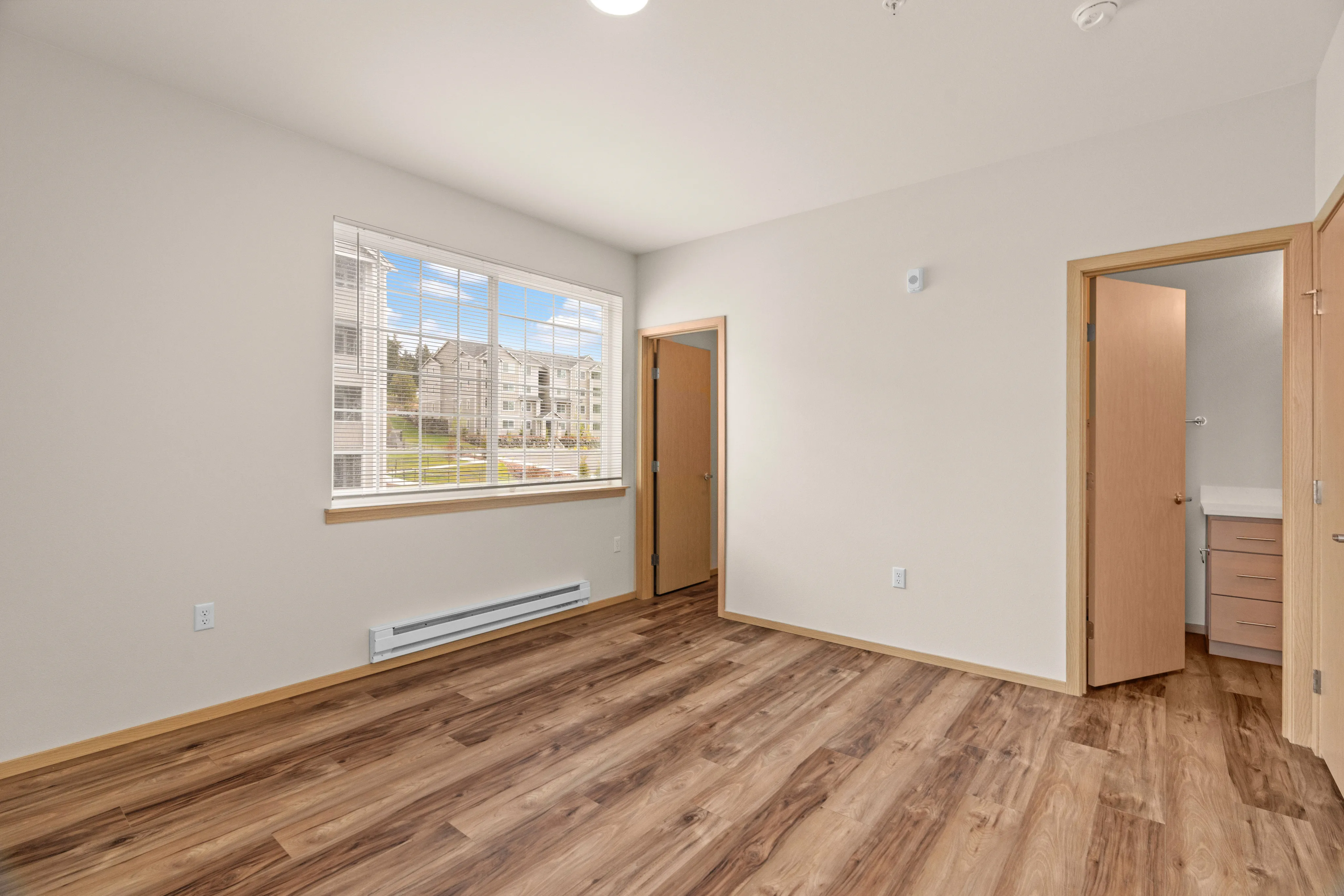 Bright and inviting bedroom with large window, modern hardwood flooring, and adjacent bathroom access.