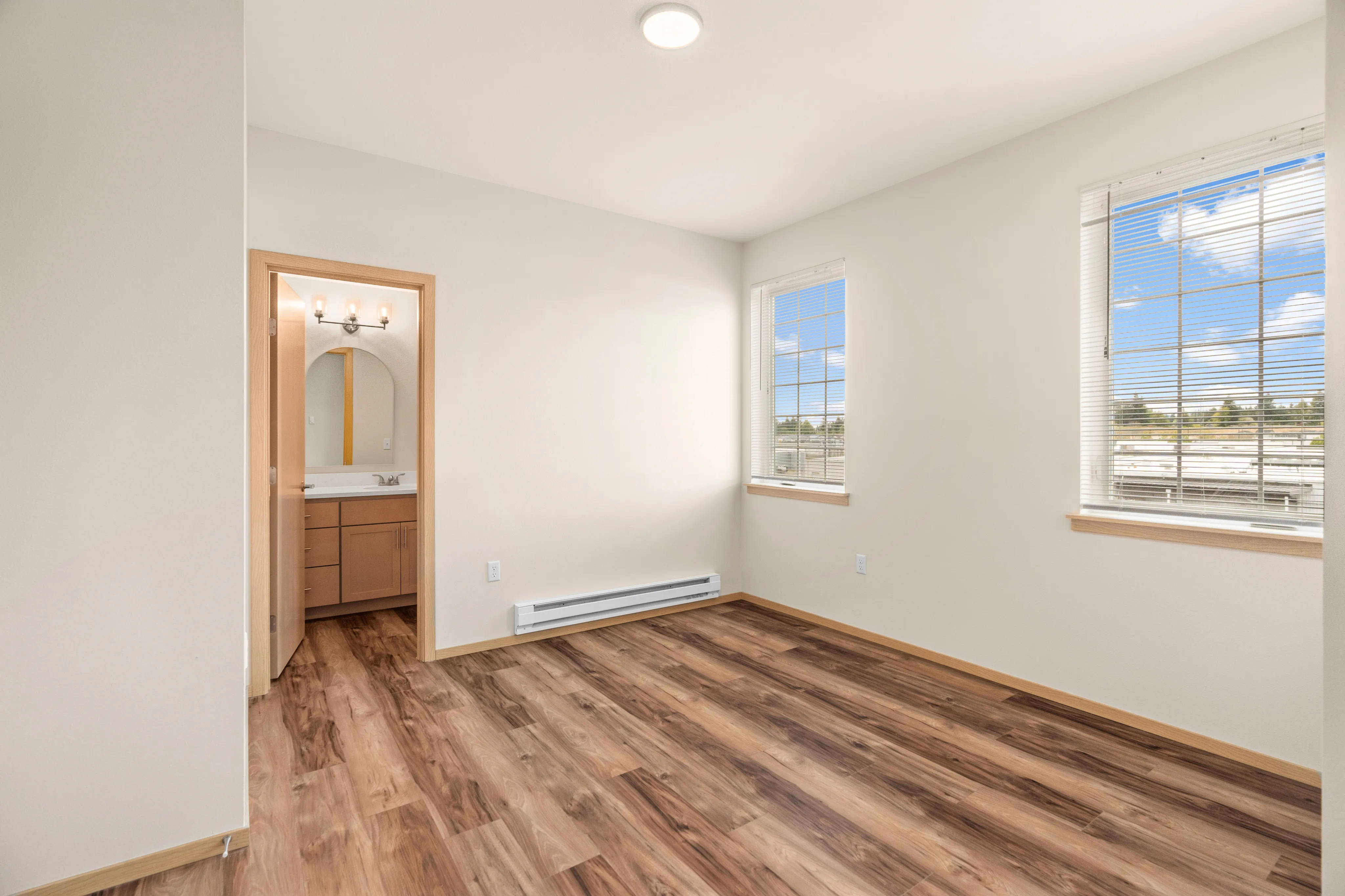Bright bedroom with wooden flooring and large windows offering natural light and scenic views, adjacent to a modern bathroom.