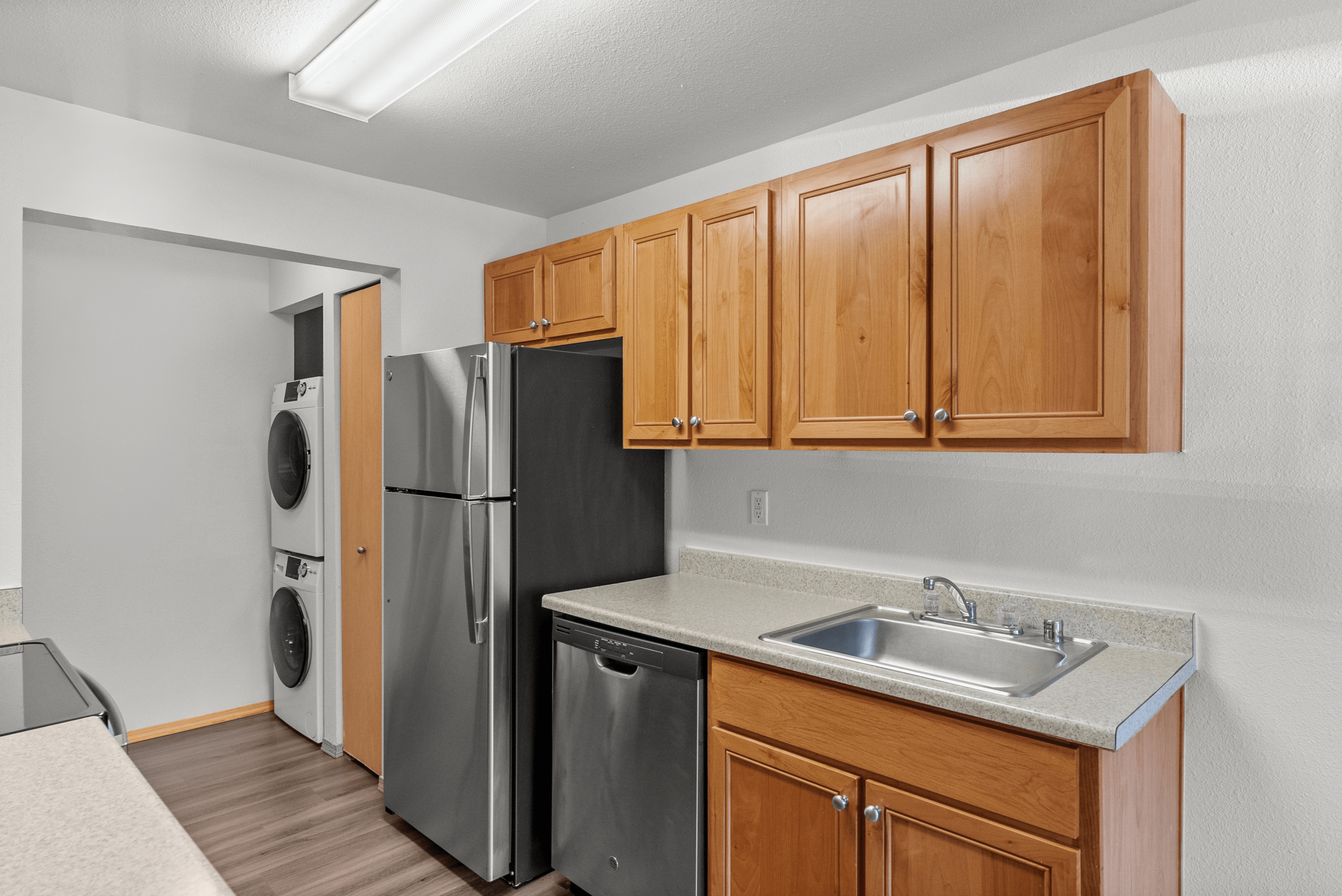 Modern kitchen with sleek stainless steel appliances, warm wooden cabinets, and in-unit washer-dryer, offering convenience and style.