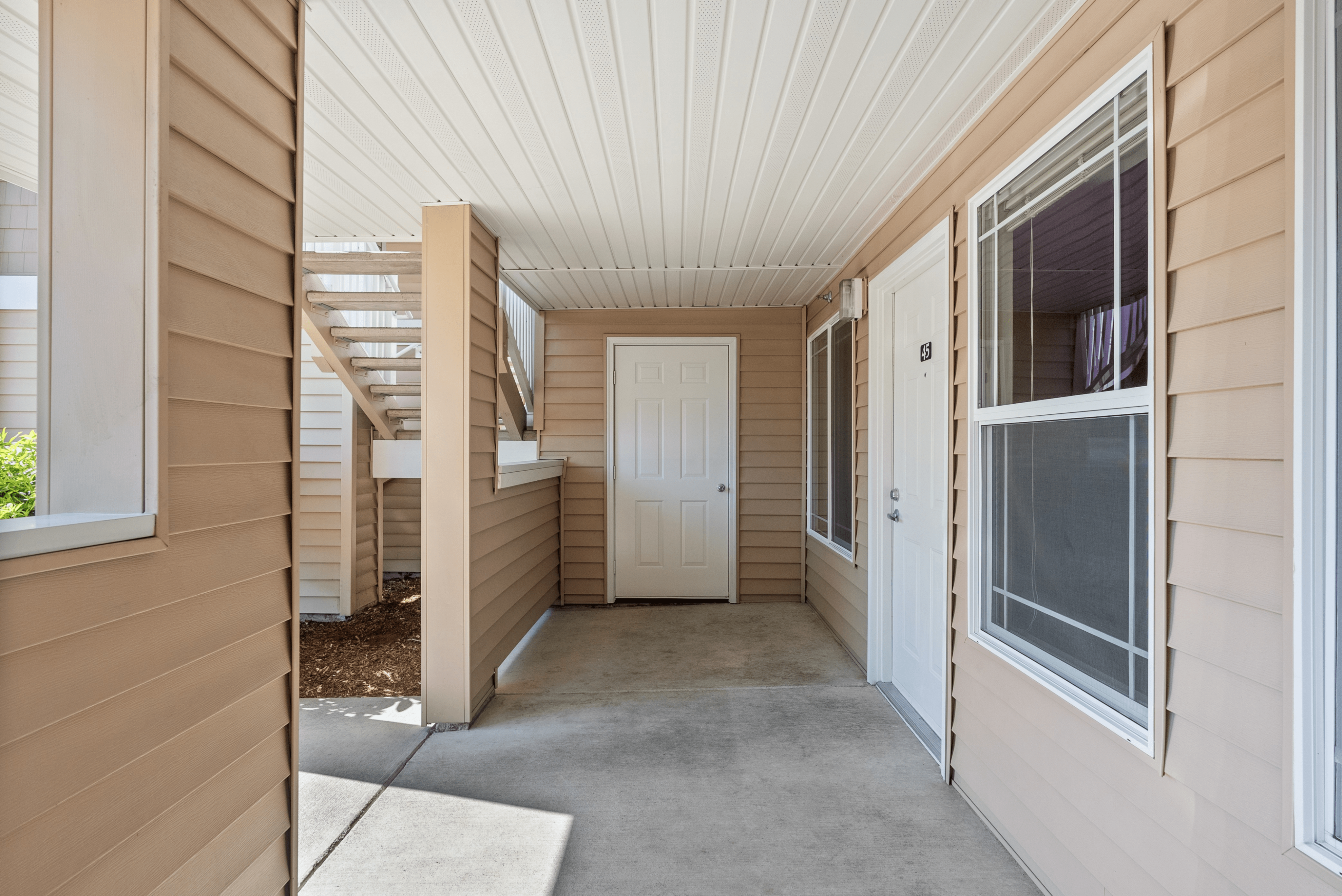 Charming apartment entrance with neutral siding, large windows, and inviting stairway access.