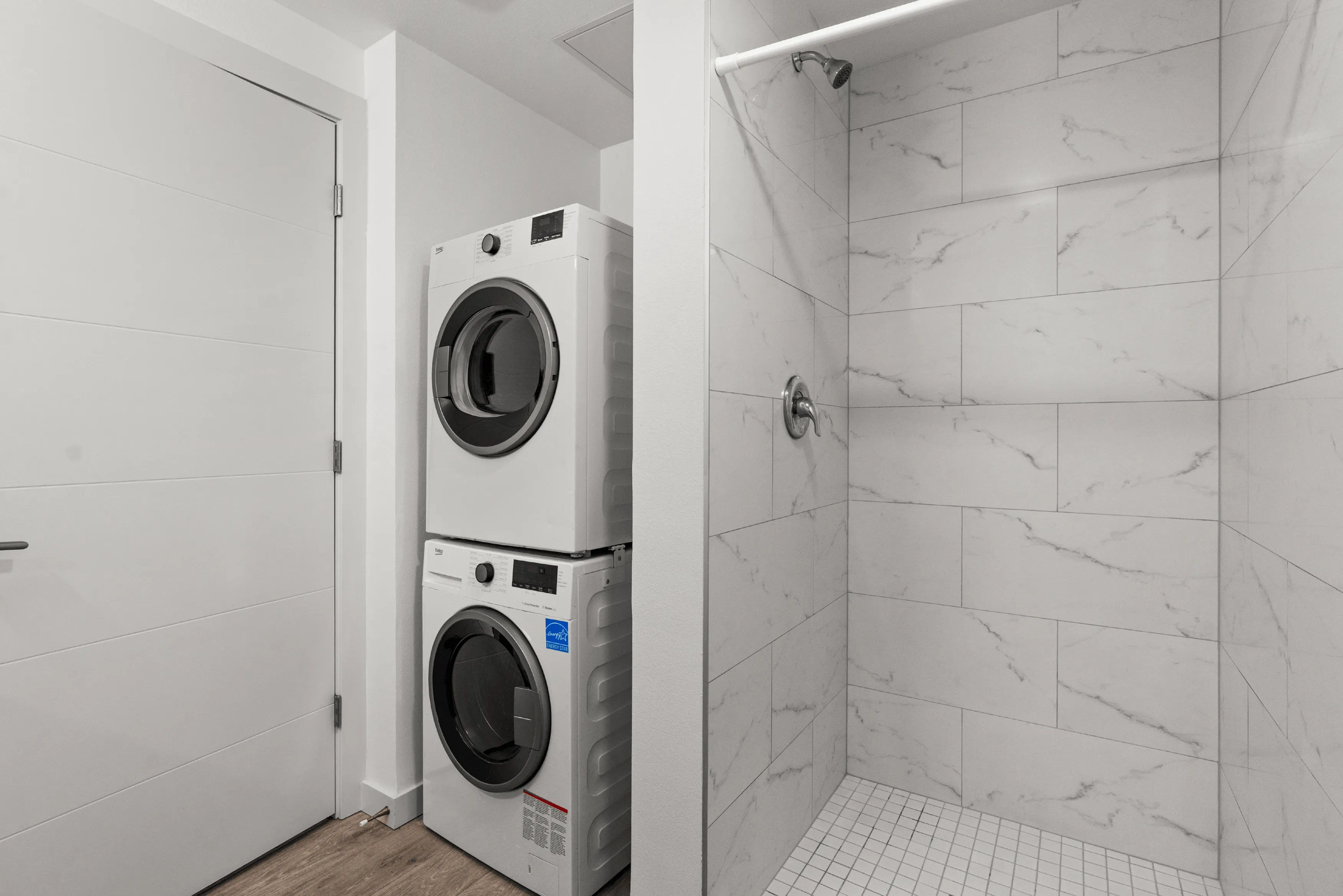 Modern laundry area featuring a sleek stackable washer and dryer next to a stylish tiled shower, offering convenience and contemporary design in a compact space.