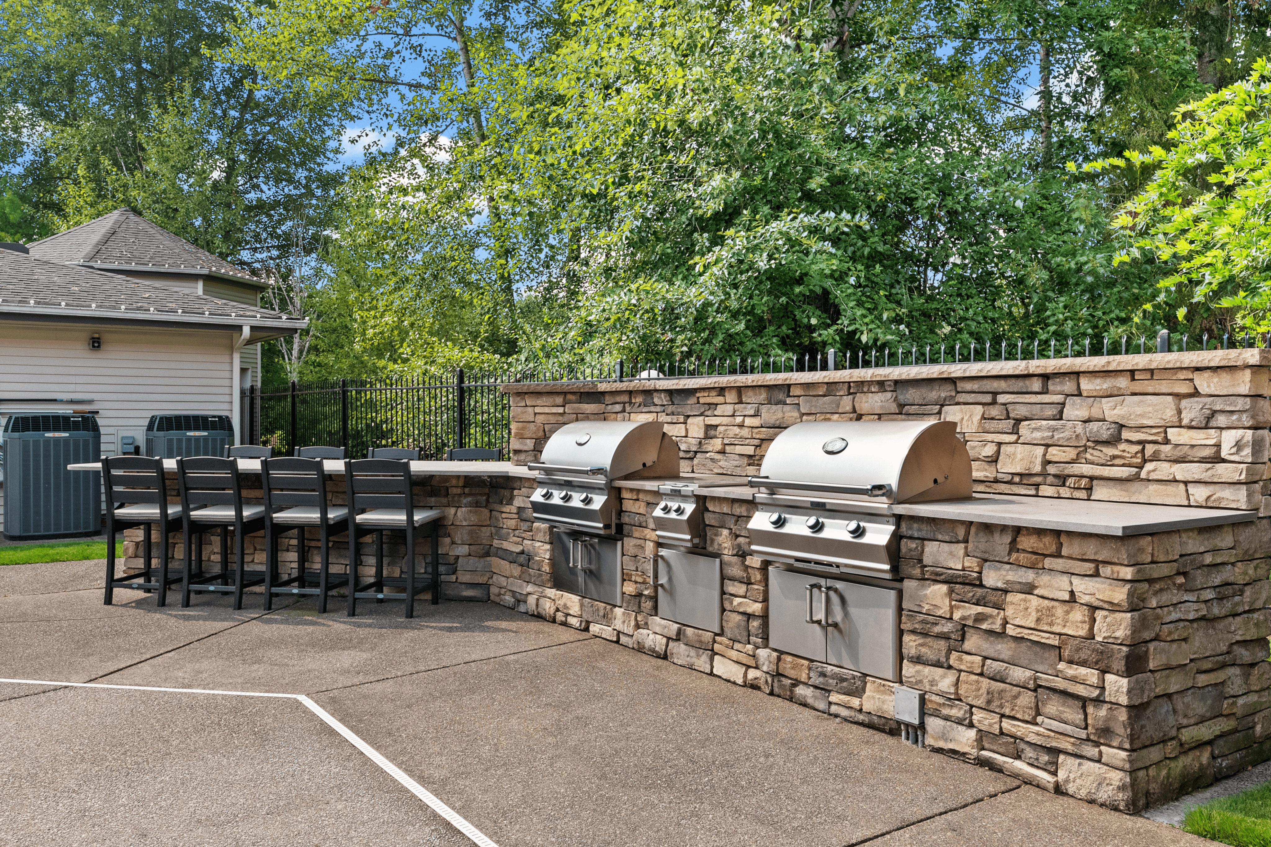 Inviting outdoor kitchen area featuring modern stone countertops, dual stainless steel grills, and stylish bar seating surrounded by lush greenery.