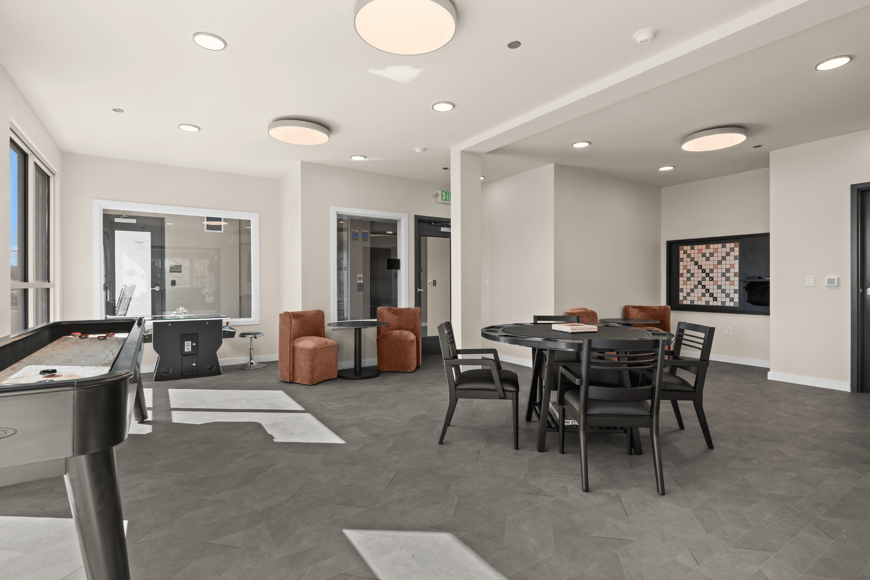 Contemporary apartment amenities room featuring stylish seating, game tables, and natural light.