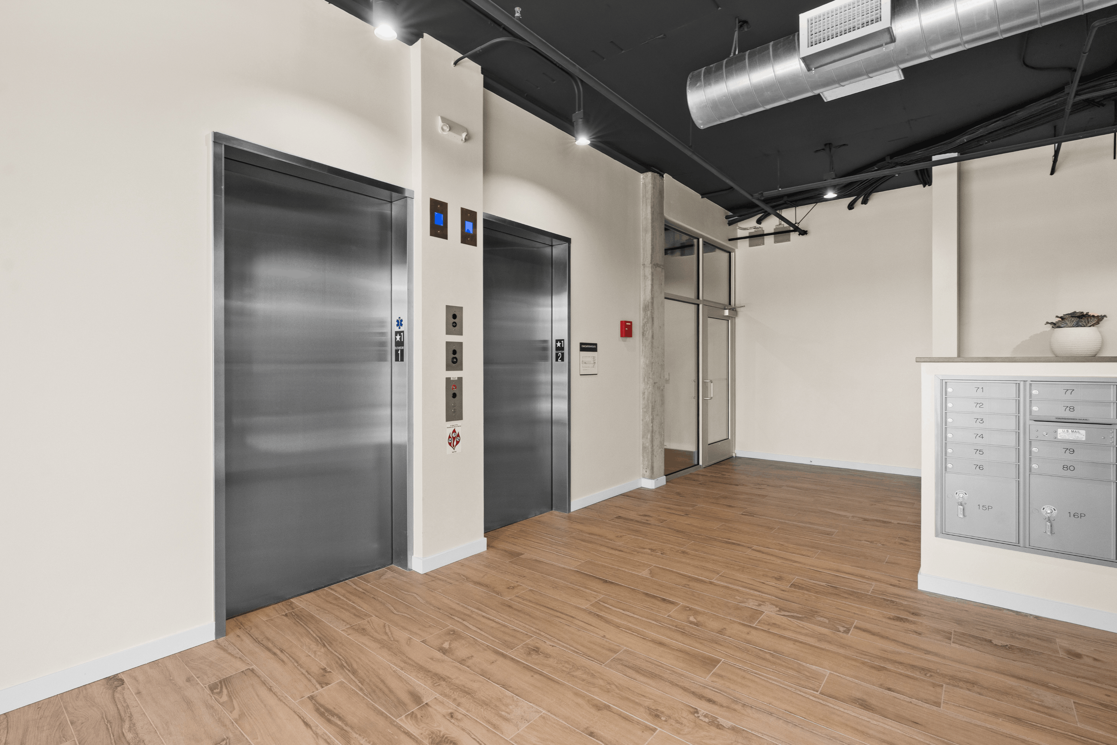 Modern apartment lobby featuring sleek elevators, warm wood flooring, and convenient mailboxes.