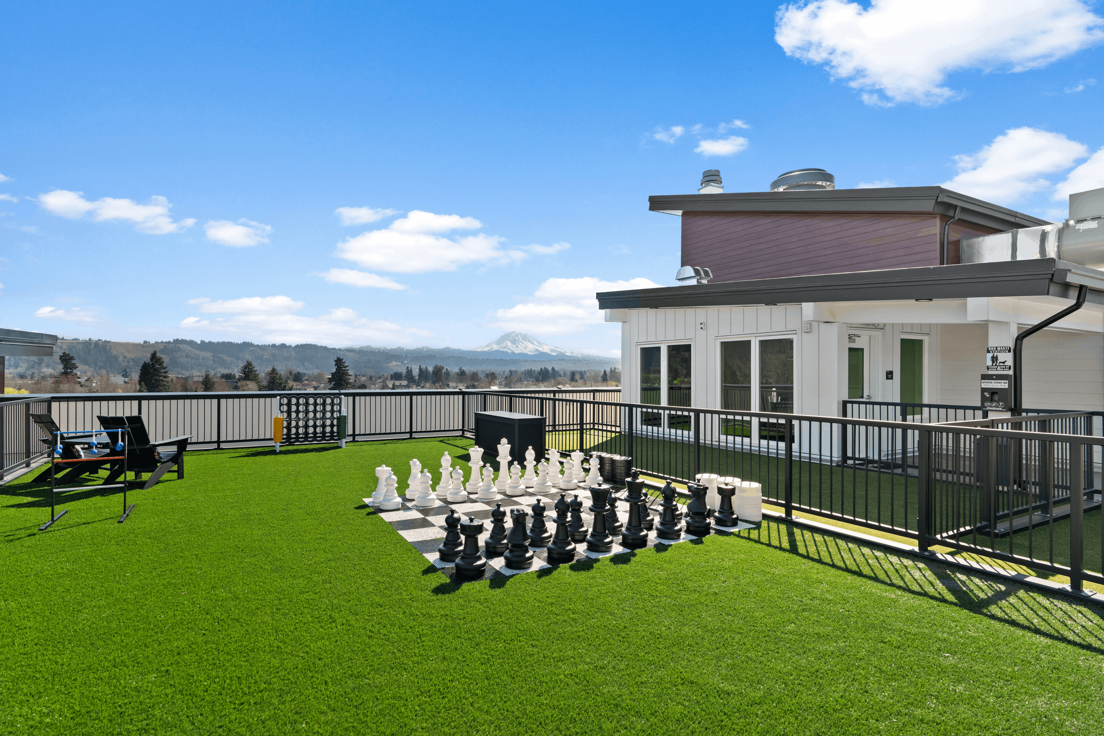 Inviting rooftop terrace with lush green lawn, large chess set, and stunning mountain views under a bright blue sky.