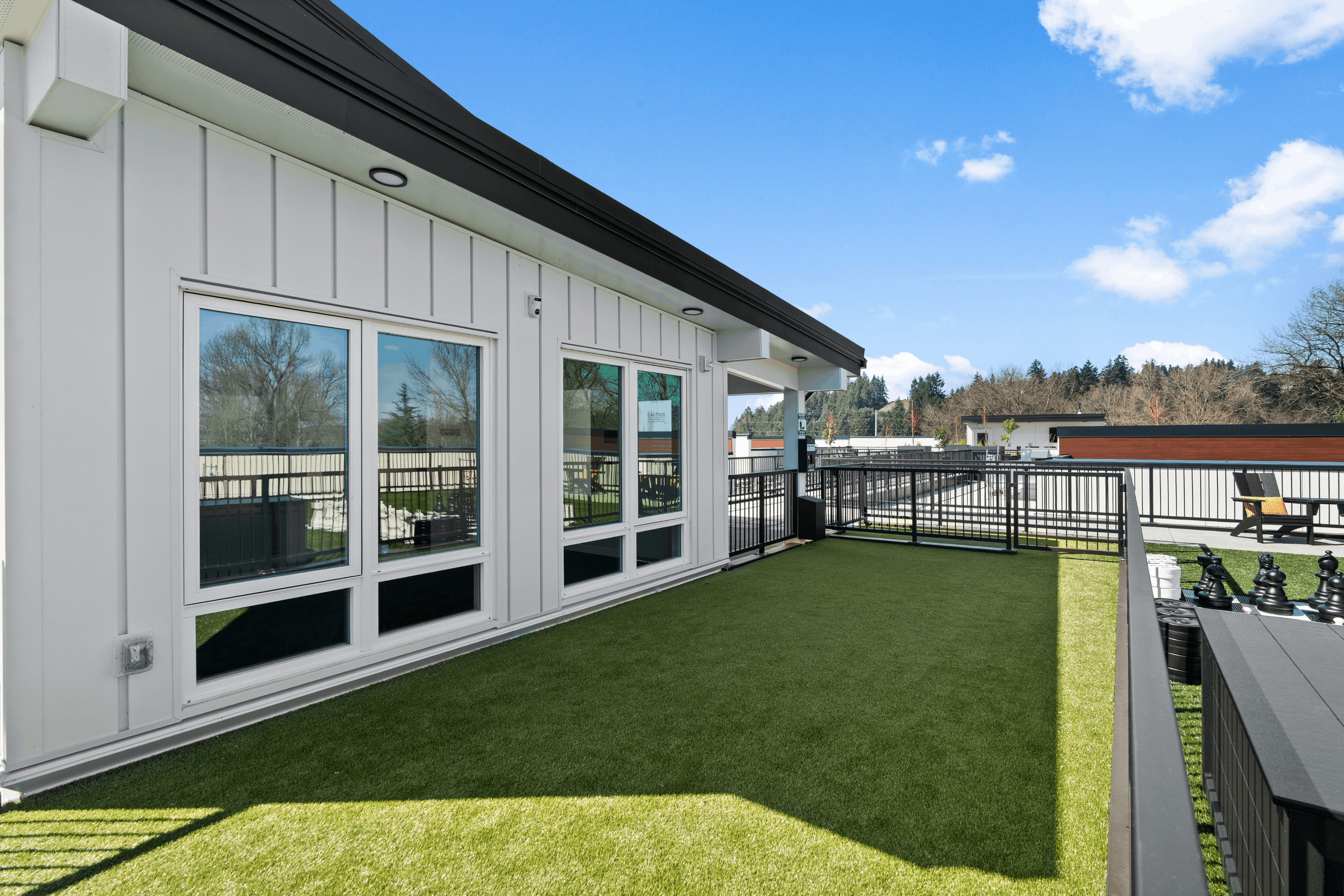 Charming rooftop terrace with lush green artificial turf, contemporary railing, and serene views of the surrounding trees.