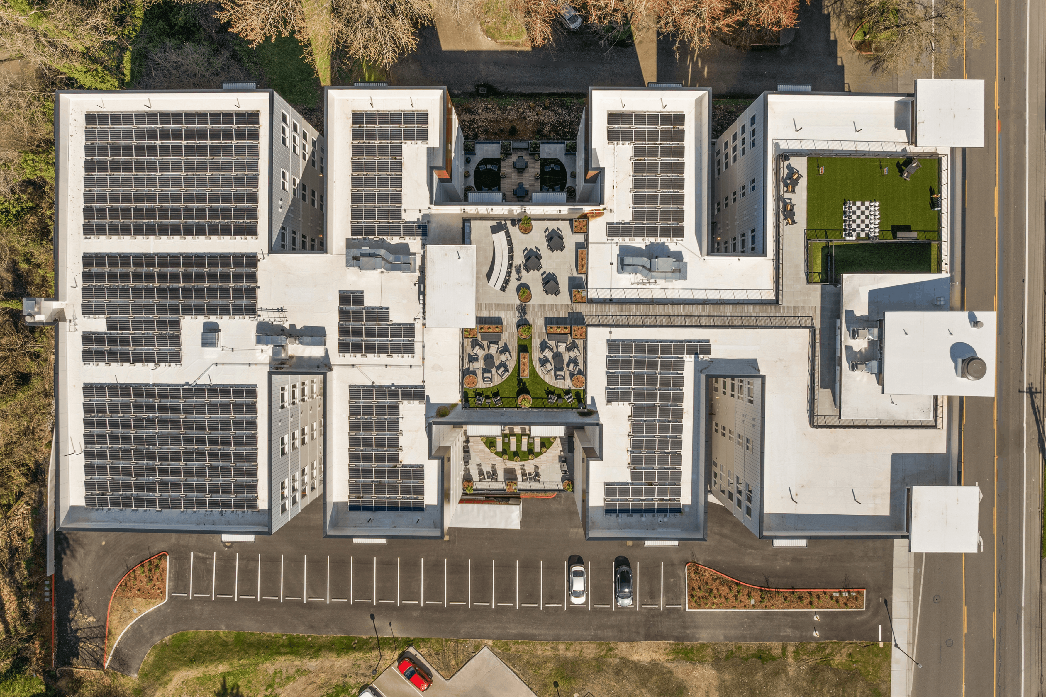 Aerial view of a modern apartment complex with solar panels, an inviting rooftop garden, and ample parking space.