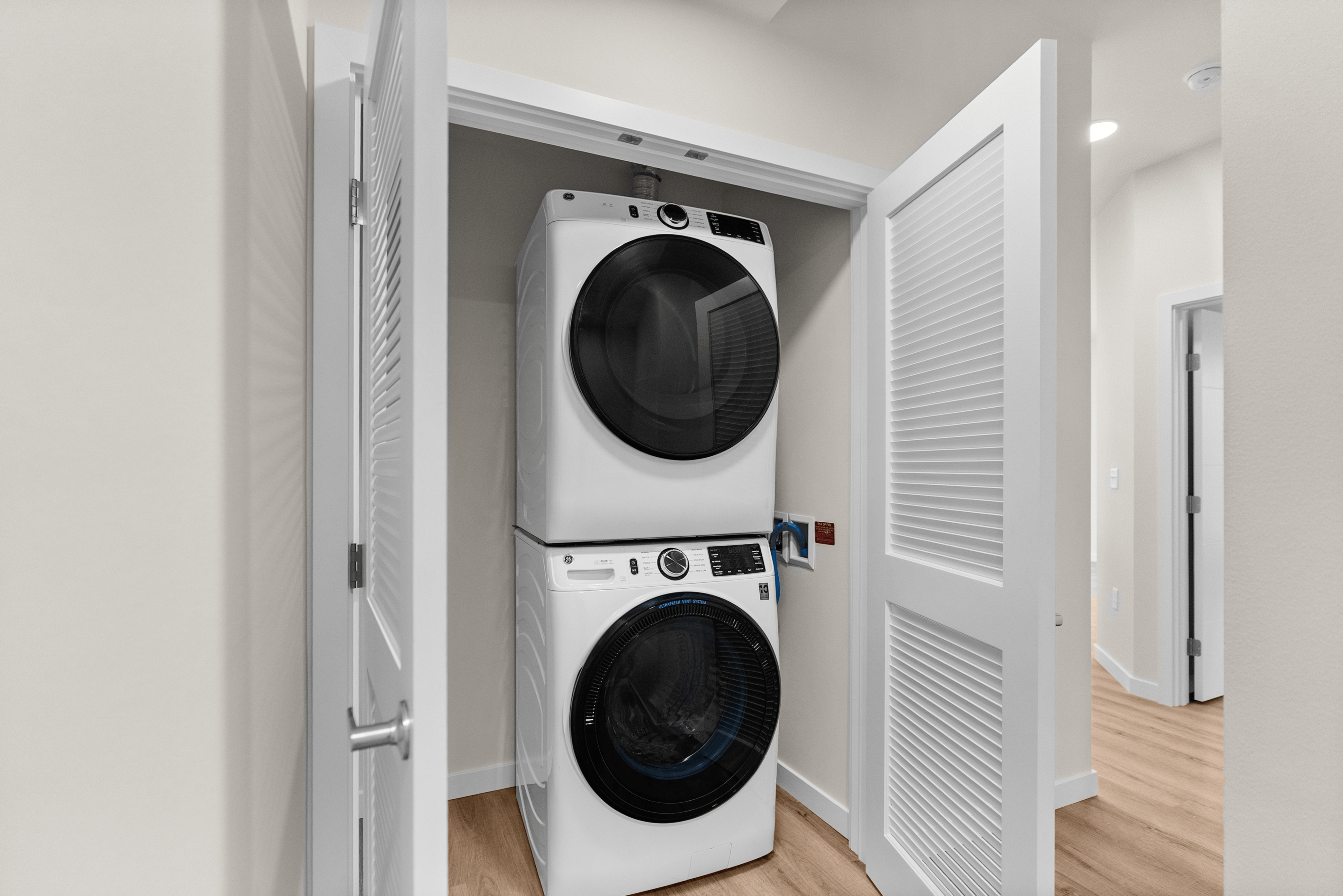 Modern apartment featuring an efficient stacked washer and dryer neatly tucked in a sleek, double-door closet with elegant wood flooring.