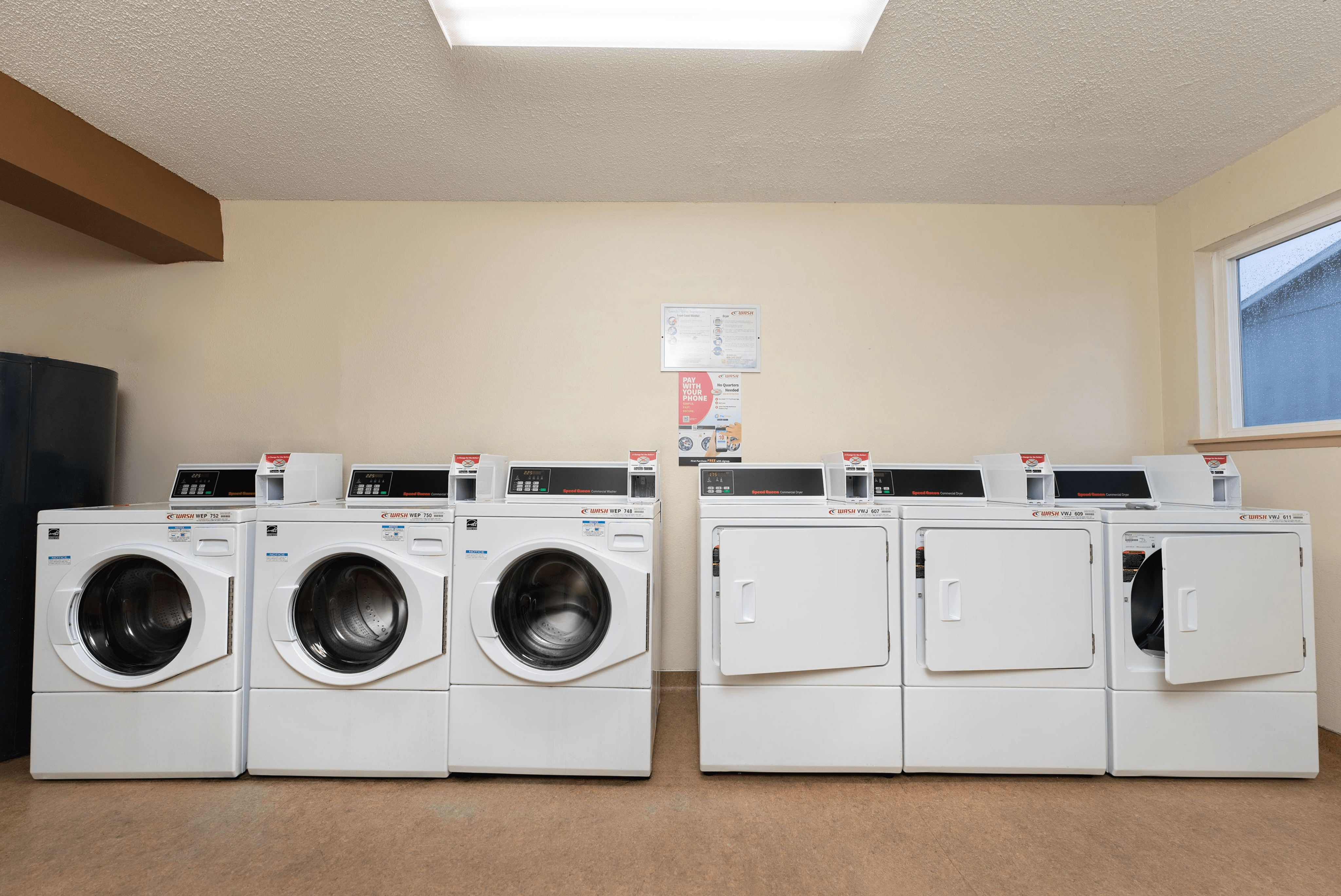 Spacious and well-lit laundry room featuring a row of modern washers and dryers, perfect for convenient living.