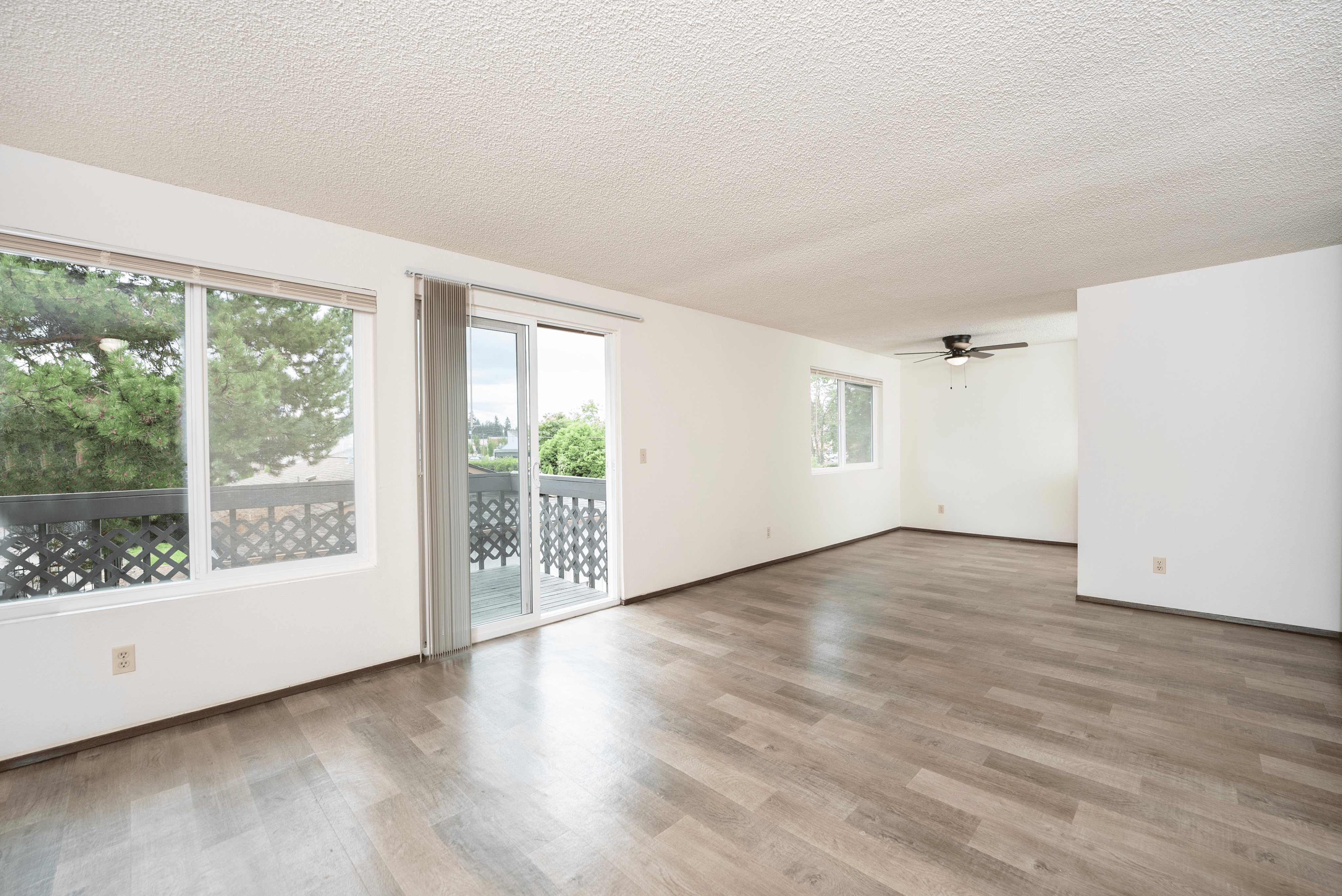 Bright and spacious living room with large windows, modern flooring, and access to a private balcony offering a serene view.