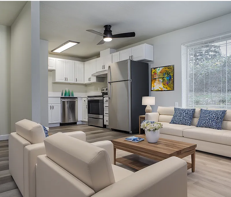 Bright open-plan living area with modern kitchen, elegant sofas, and a large window.